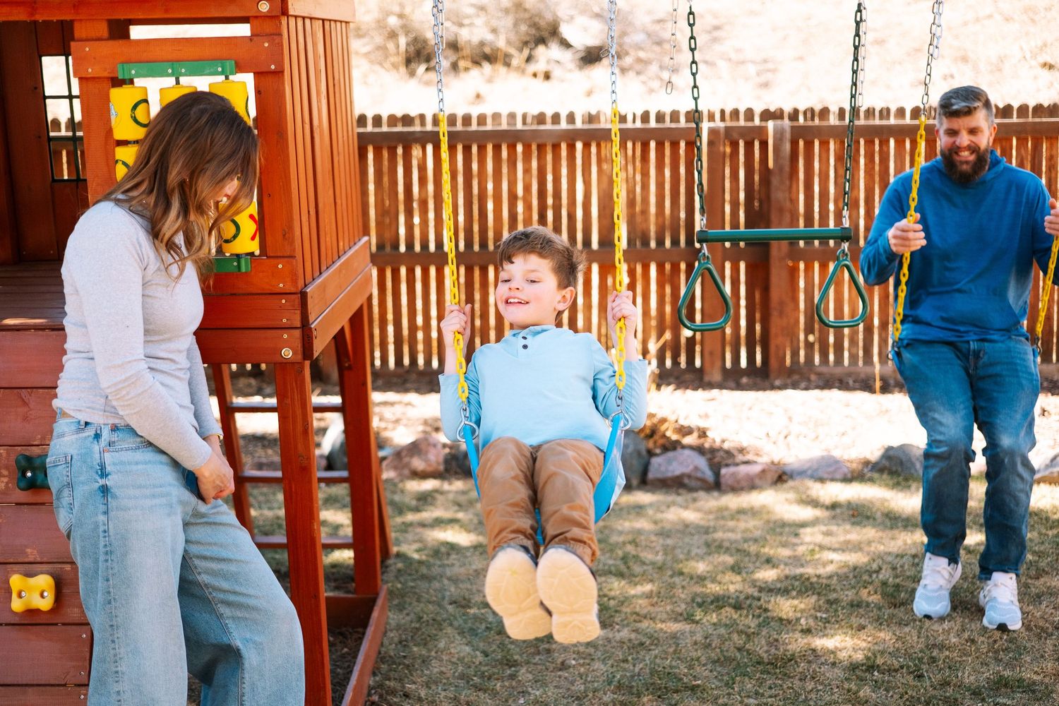 Documentary session photo of mother, son and father playing on the playground in their backyard.