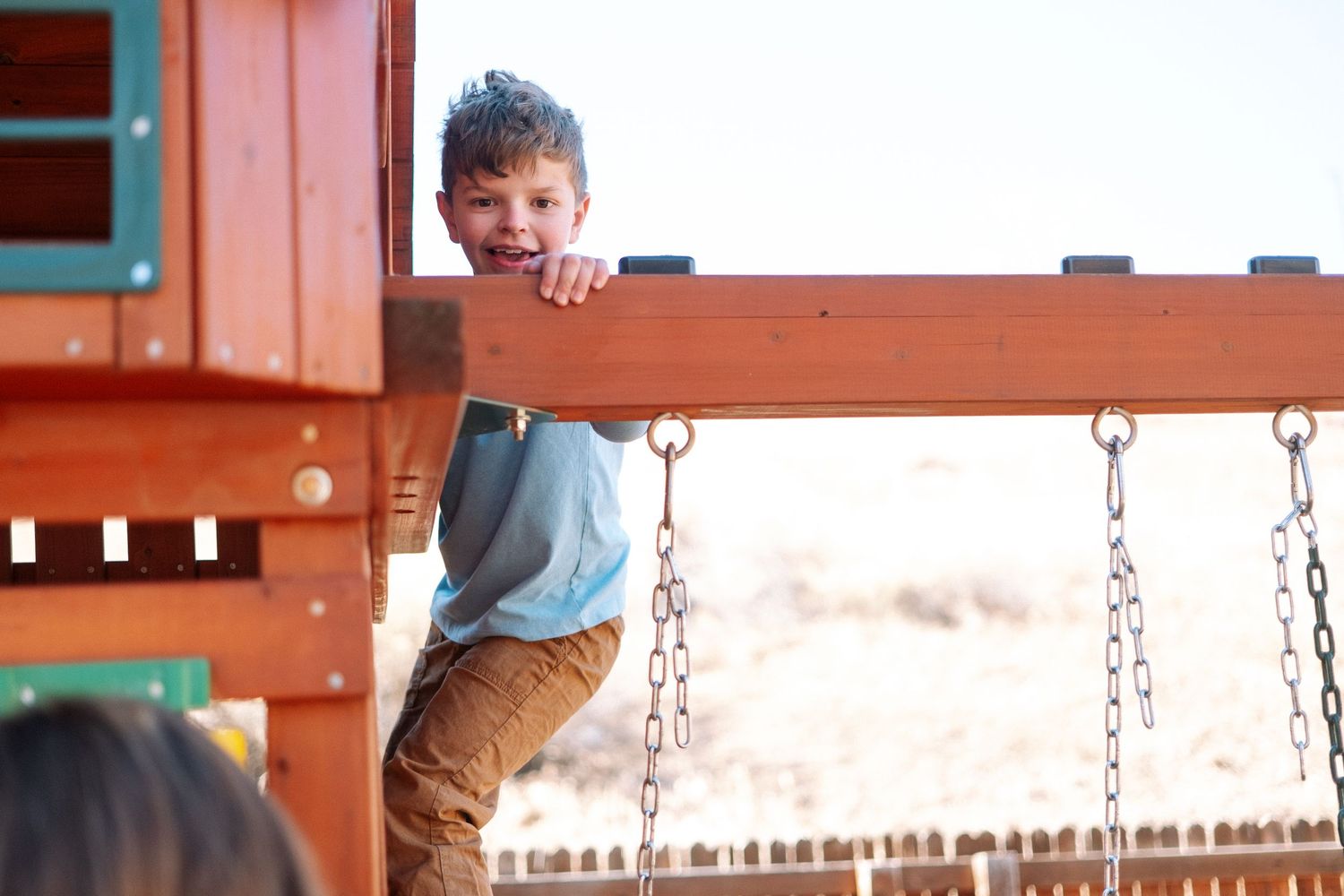 Boy perched high on climbing equipment of backyard playground.