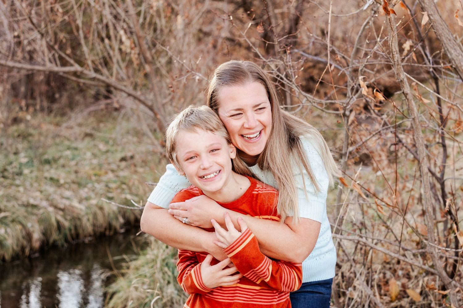 Mother and son smiling beside the creek at Matthews / Winter Park in Golden, Colorado, during a family photo session.
