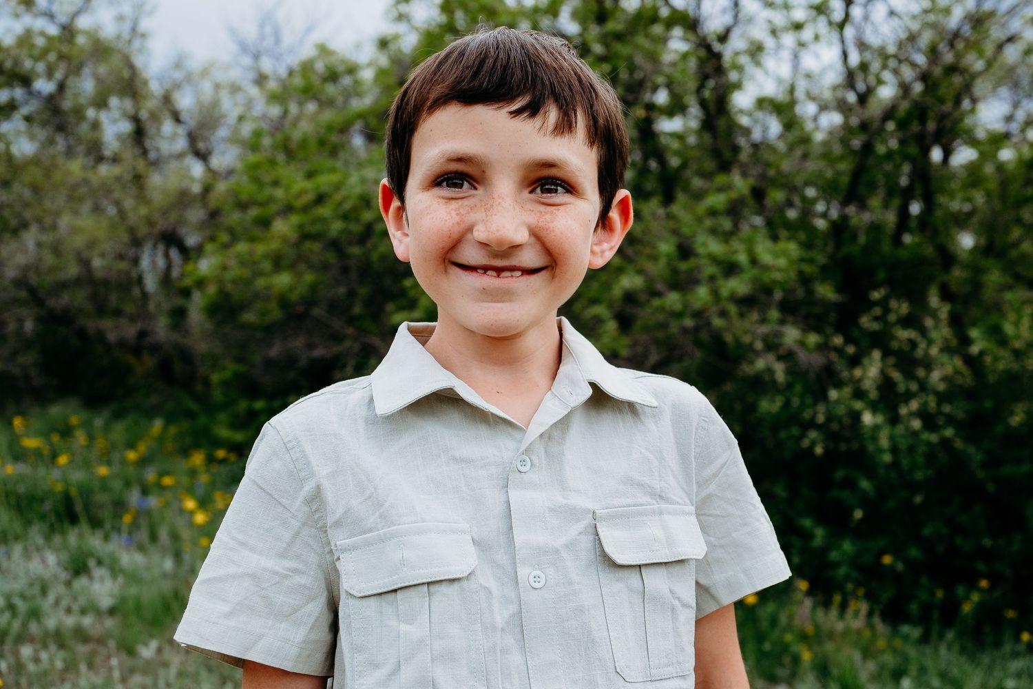 Portrait of young boy smiling, greenery and flowers in background.