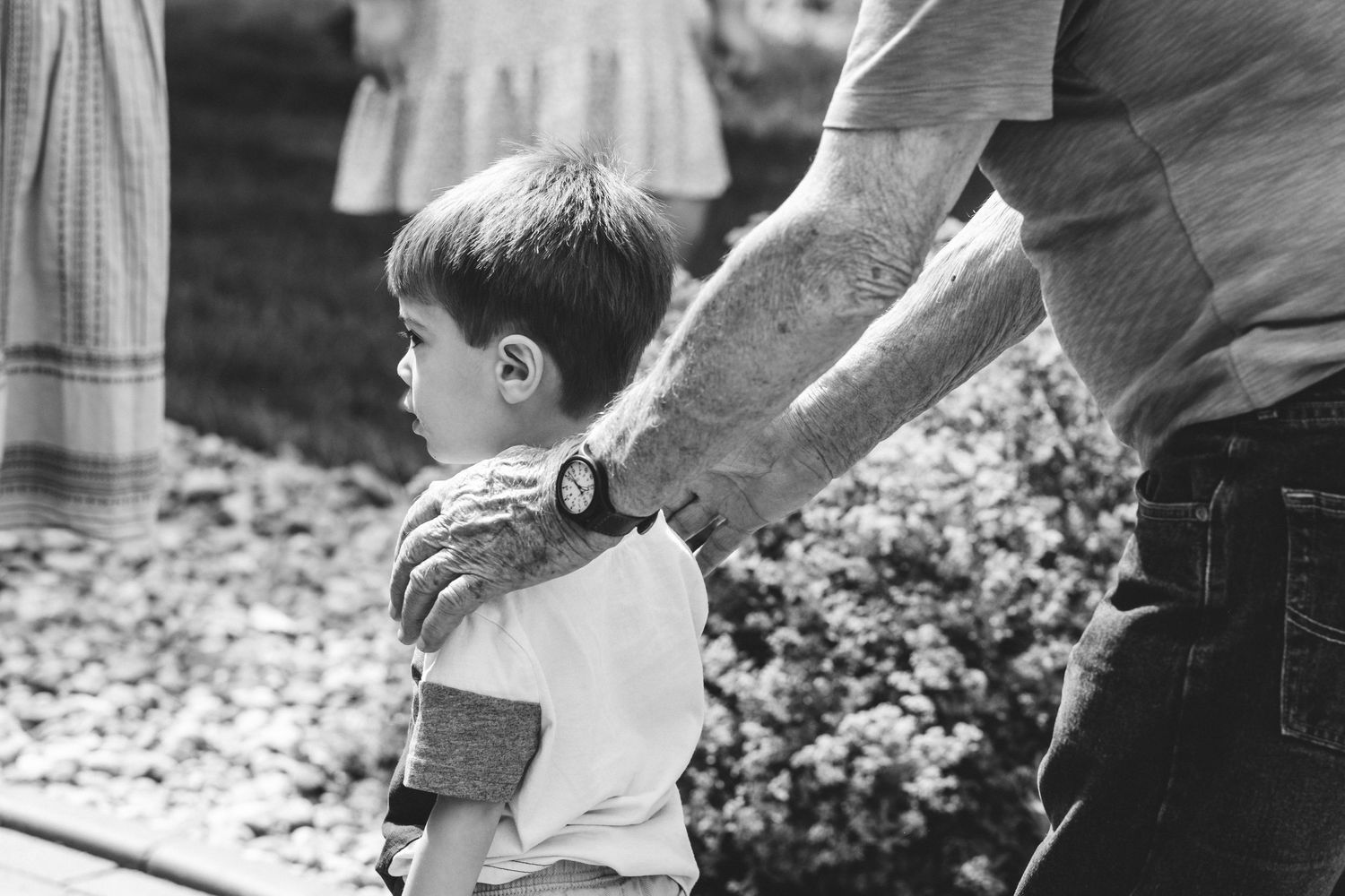 Black and white photo of great grandpa resting hands on great grandson's shoulders, guiding him along a path.