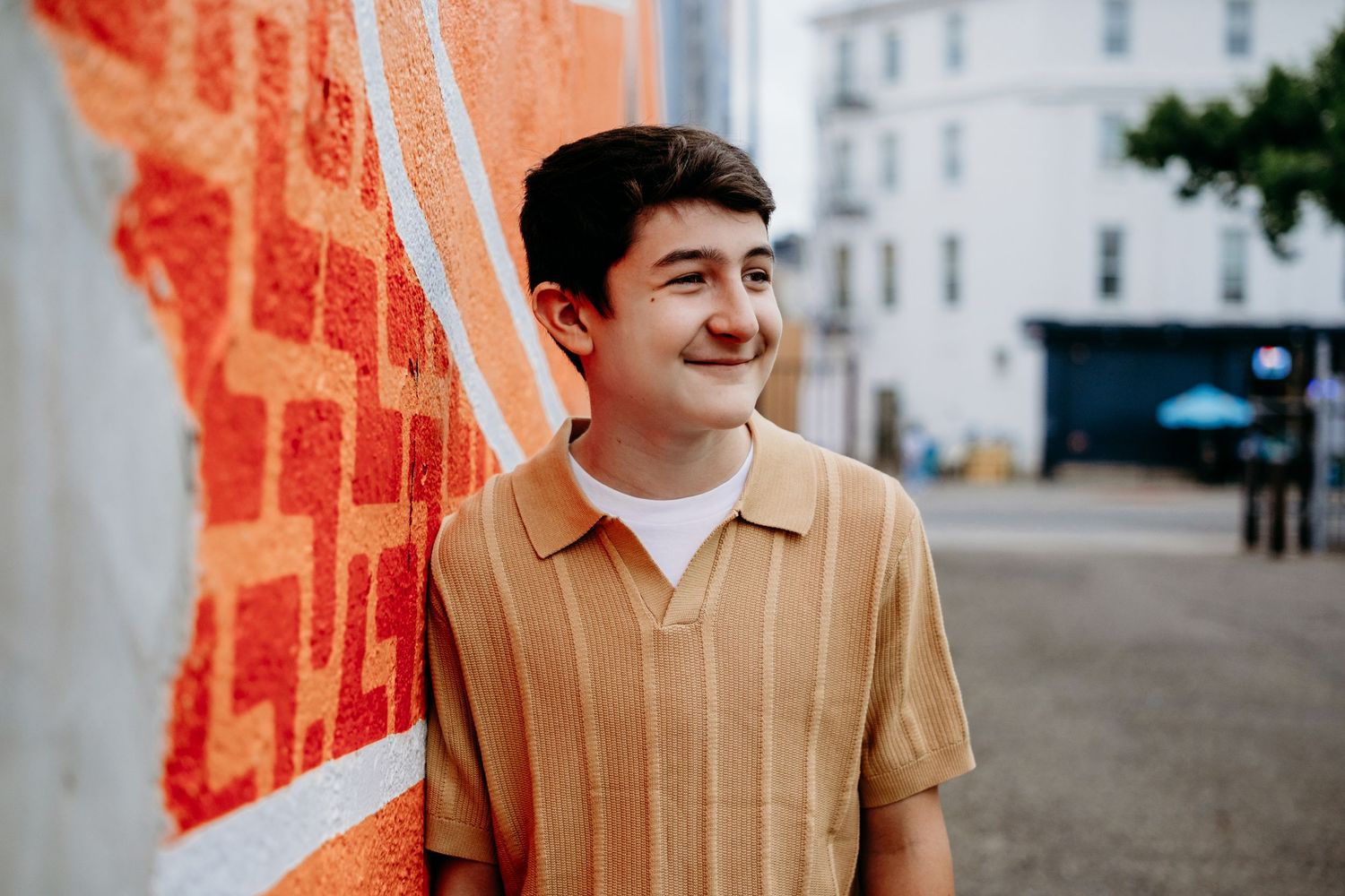 Teen portrait, leaning against colorful wall, smiling.