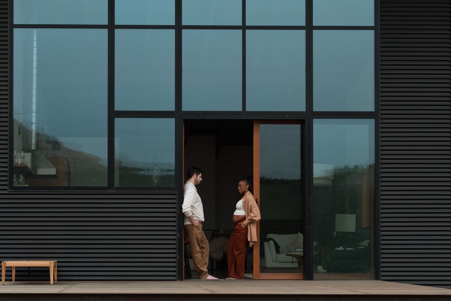 Mother and father to be perched inside door frame, surrounded by stunning glass at Boulder cabin rental.
