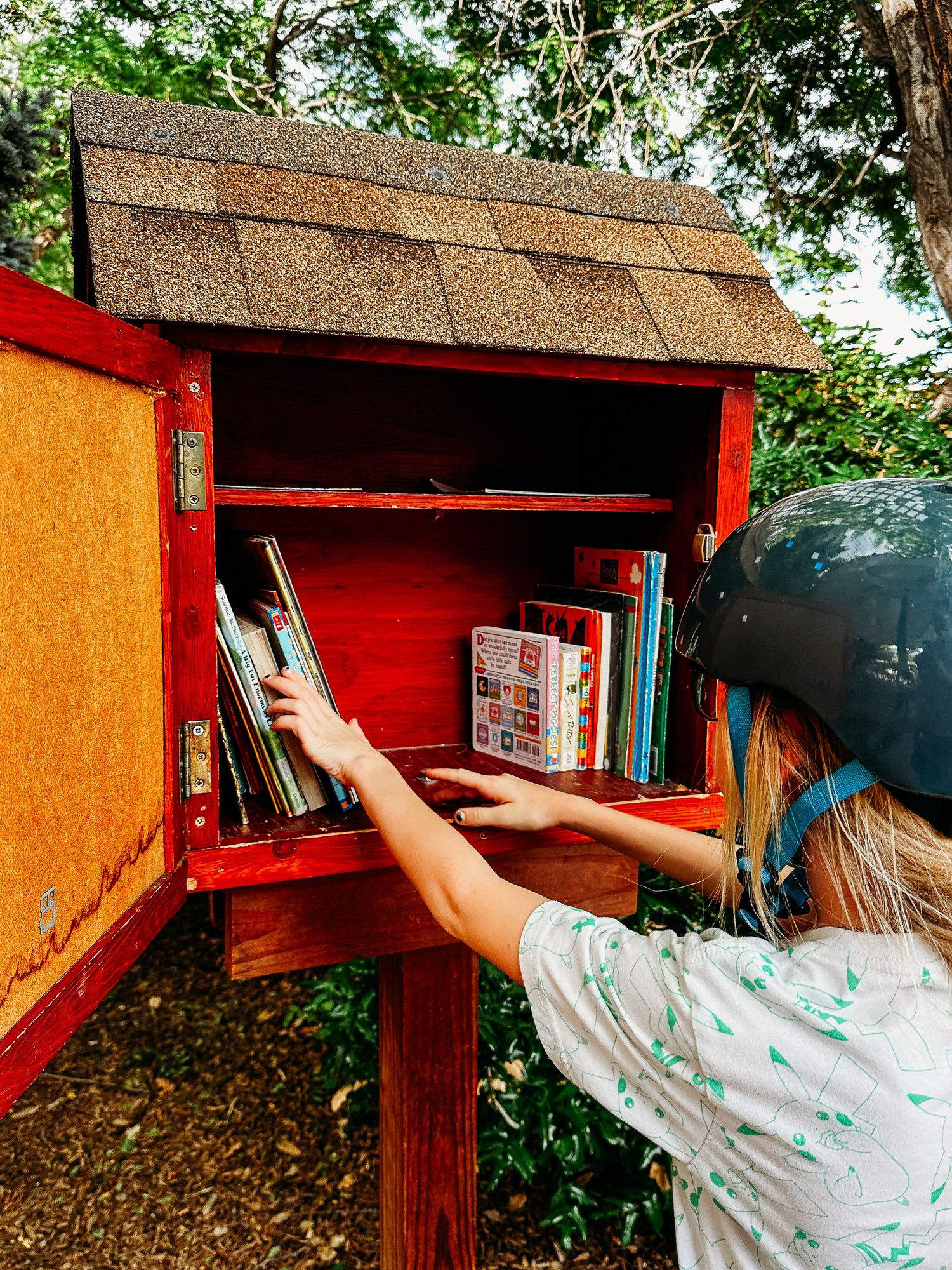 Girl adding book to neighborhood little library box.