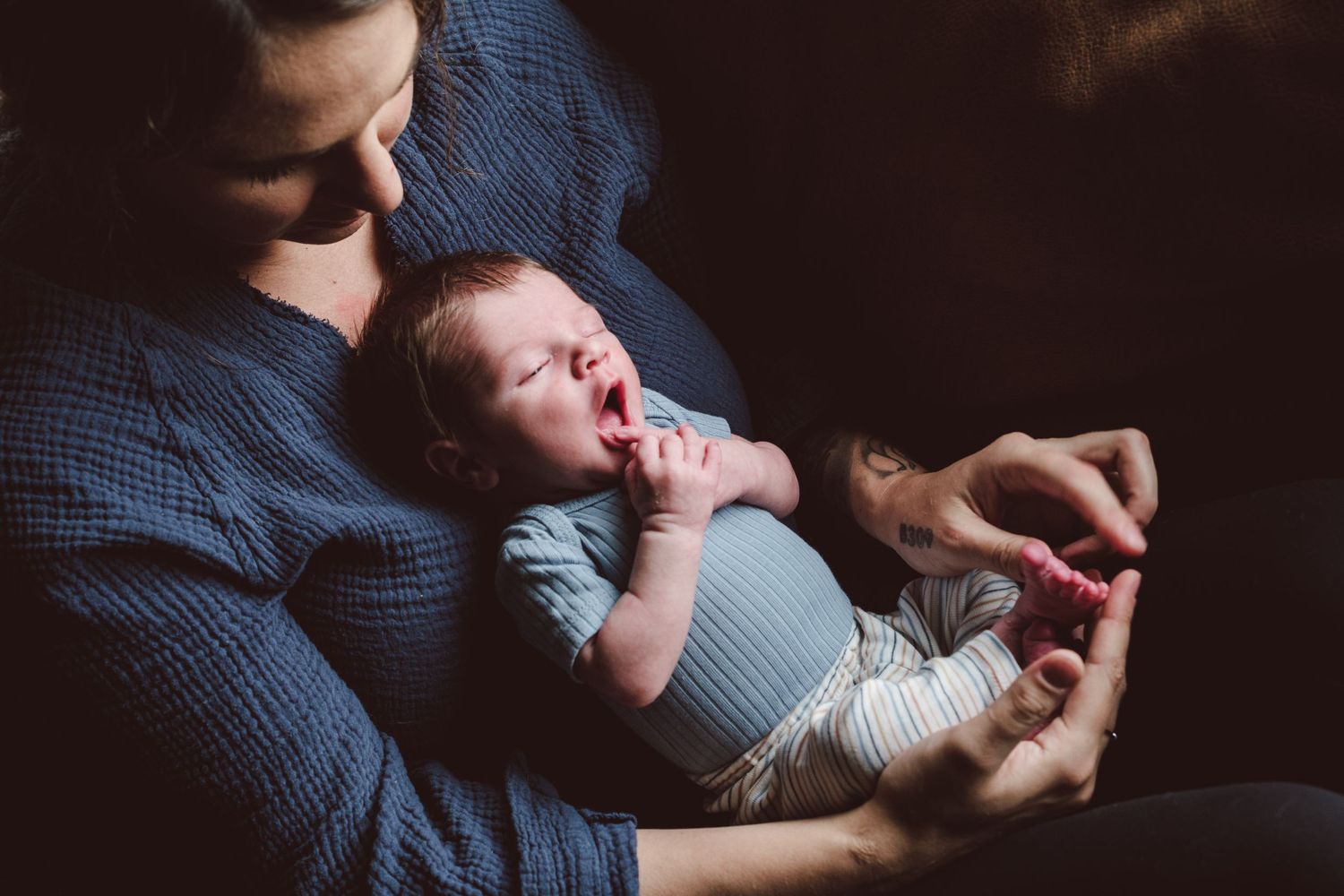 Moody close up of mother holding newborn on her chest, mom is playing with newborns toes.