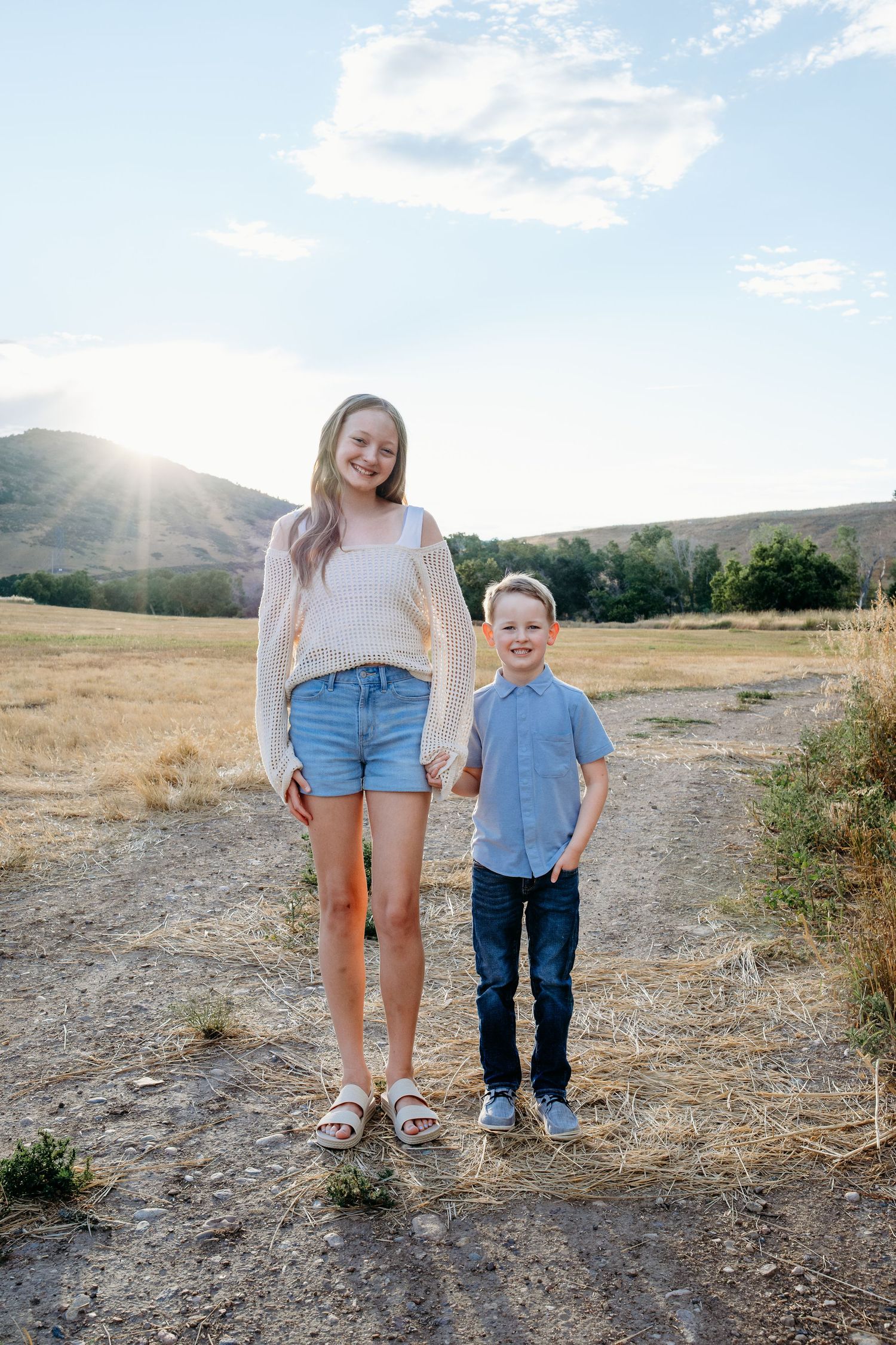 Brother and sister smiling in field at Hildebrand park with blue skies and foothills in background.