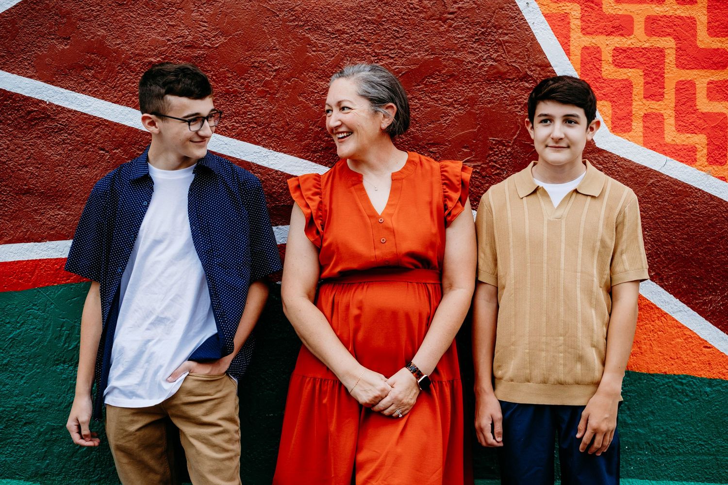 Mother surrounded by two teen sons, all smiling against a colorful mural in Downtown Fort Collins.