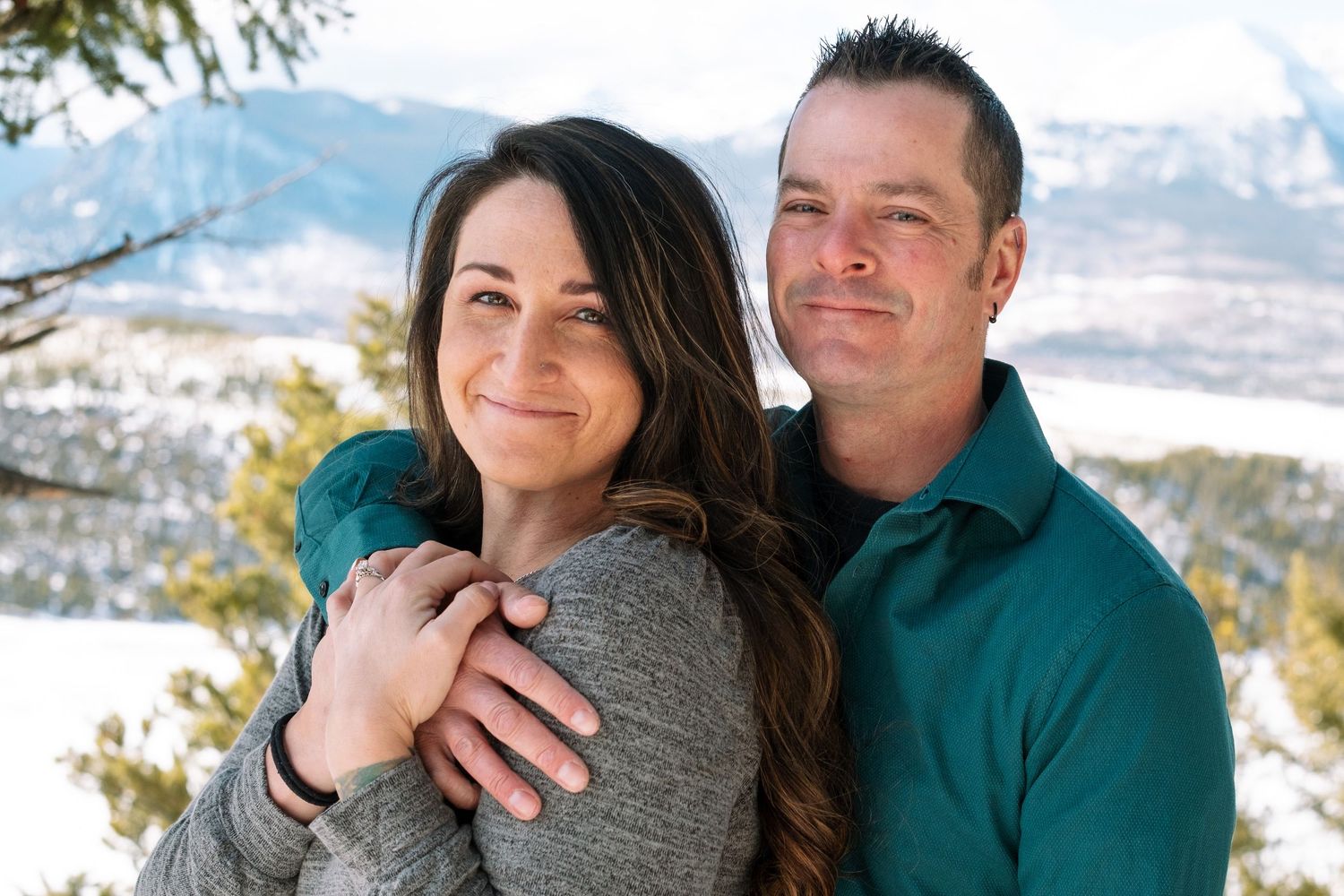 Couple posing and smiling at the camera, man is embracing woman, hugging her closely during engagement photo session near Dillon, Colorado.