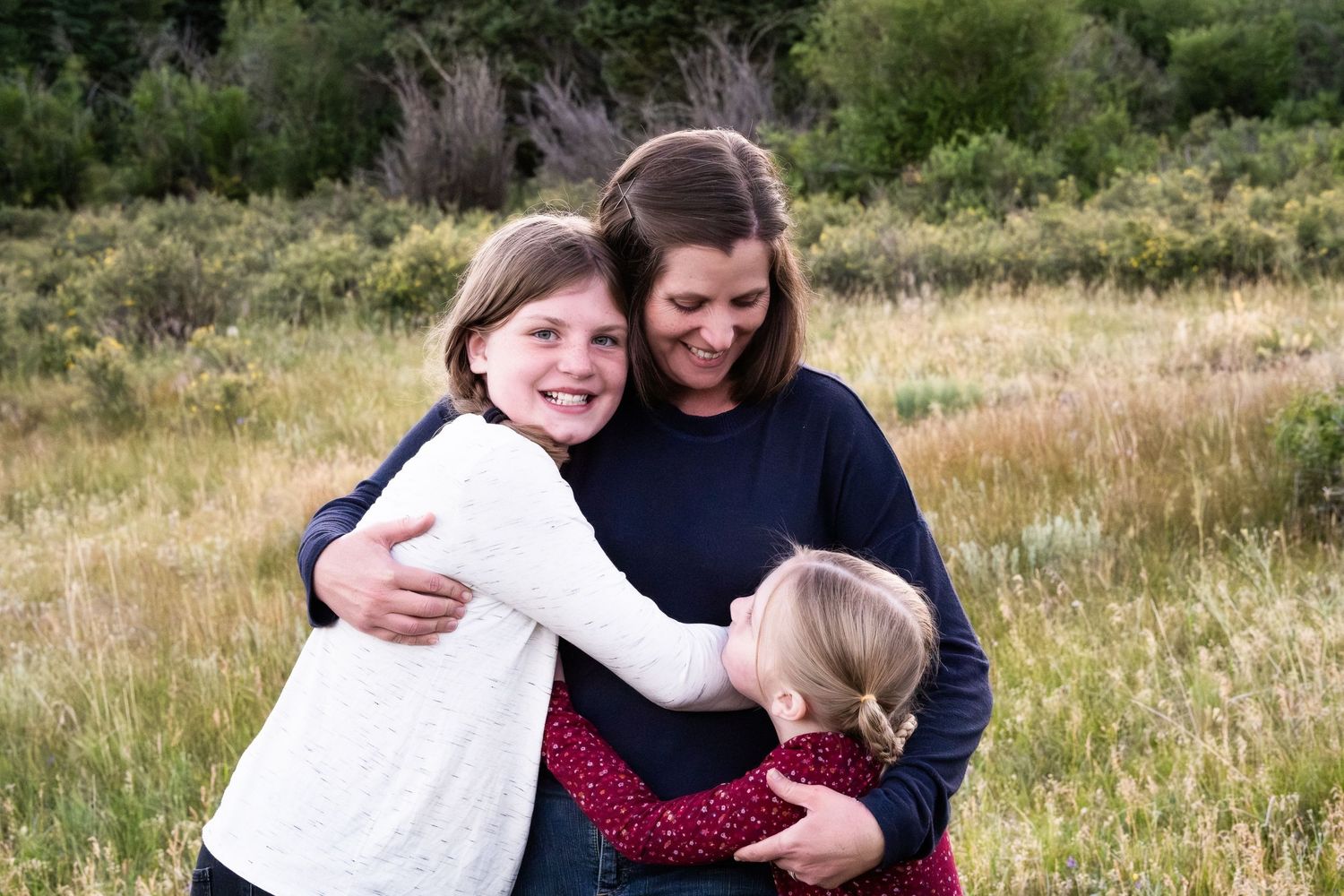 Mother standing with two daughters in mountain meadow in mountains of Colorado.