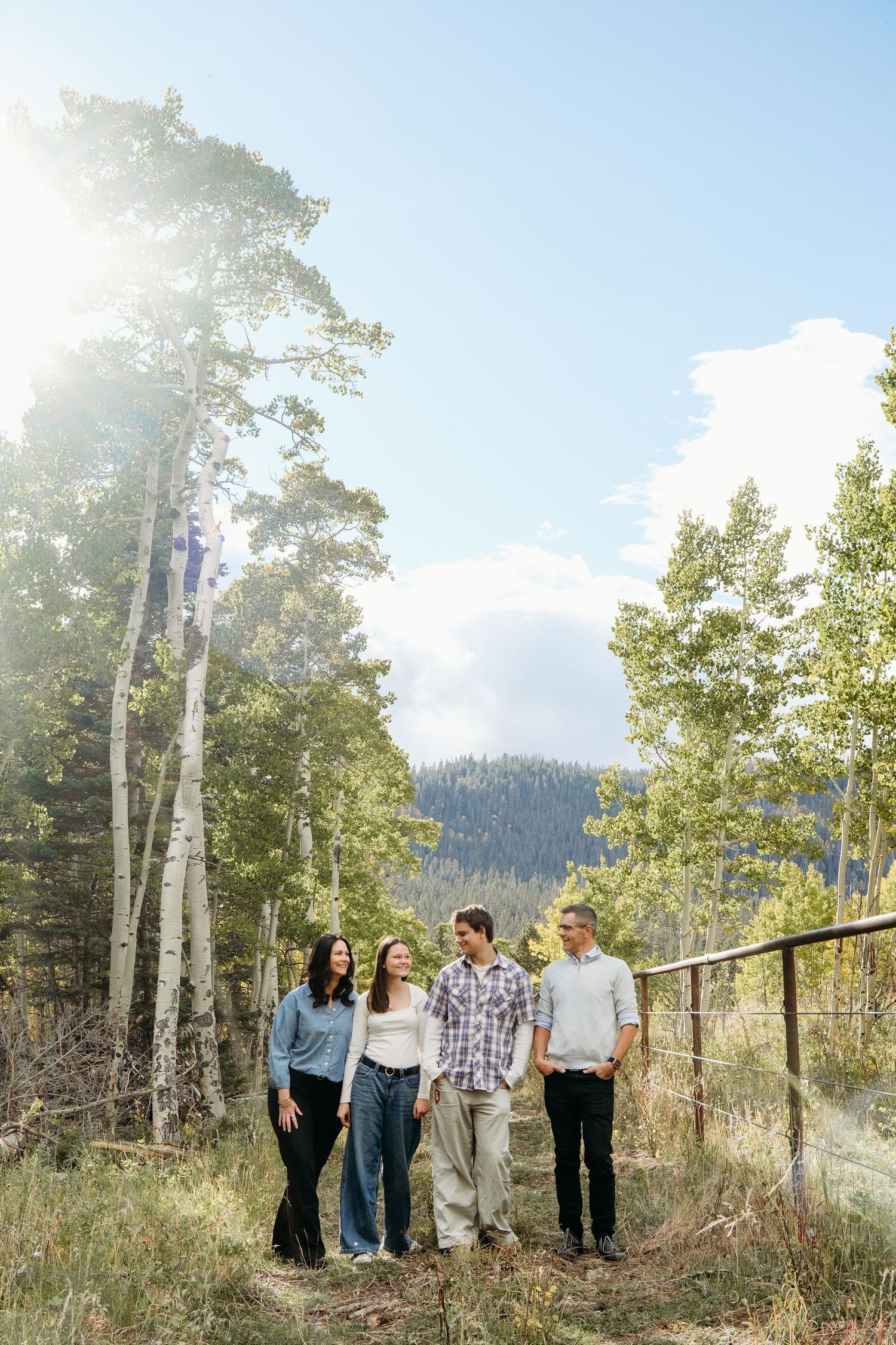 Family with teenagers in Colorado mountains, standing on path, sun flare peaking through aspens.