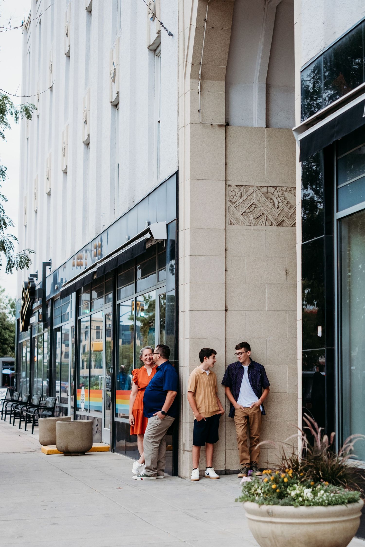 Mother, father, and two teenage sons standing on corner of multi story building with stunning architectura features in downtown Fort Collins