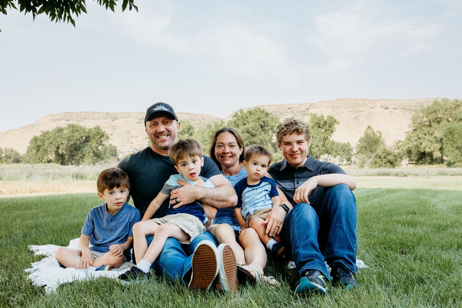 Posed portrait of family of two parents and four sons sitting on grass with foothills in the background in Golden, CO.