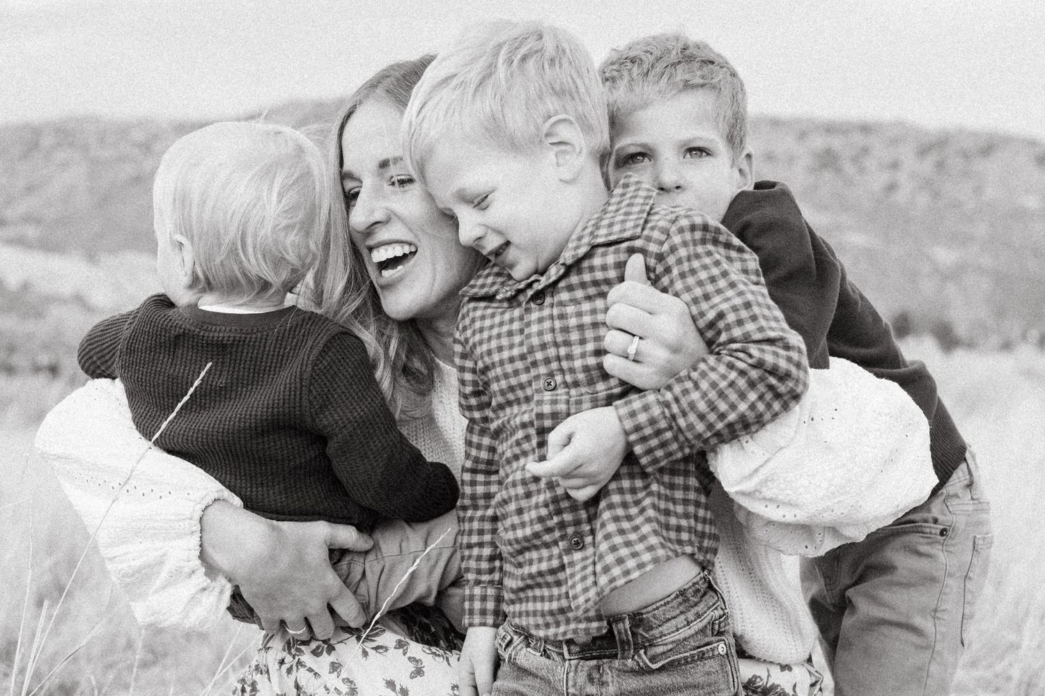 Black and white of mother holding three young sons, mother smiling.