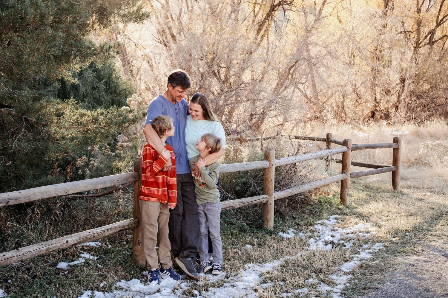 Family standing together by a wooden fence at Matthews / Winter Park in Golden, Colorado, with foothills and soft winter light in the backgr