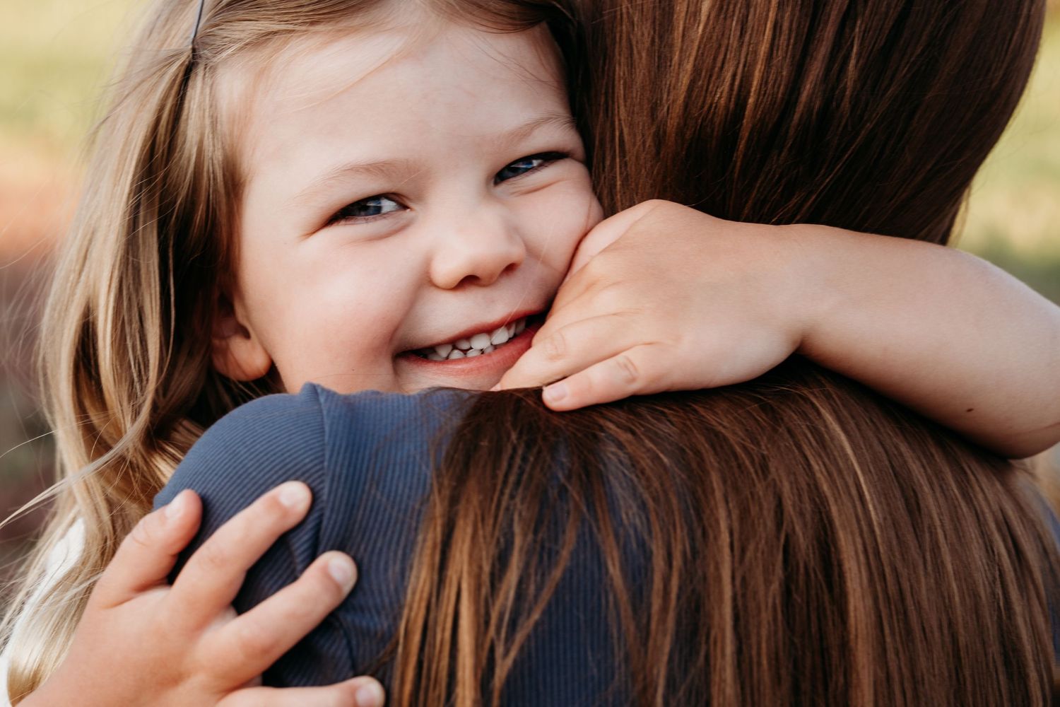 Close up of young girls face and she tightly holds onto mother's neck.