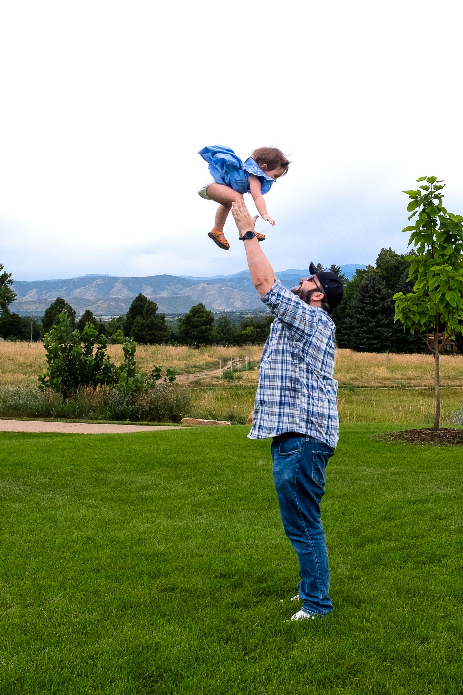 Uncle playfully tossing niece in the air at park, mountain fiews.