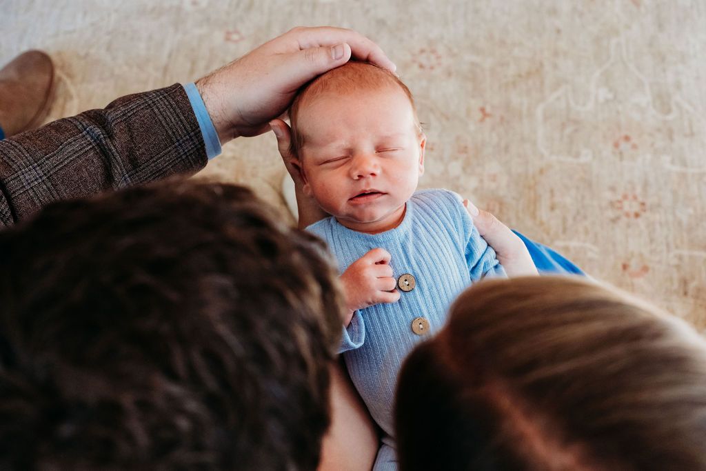 Overhead view of mother and father sitting close together, holding newborn between them, father gently caressing newborn's head.