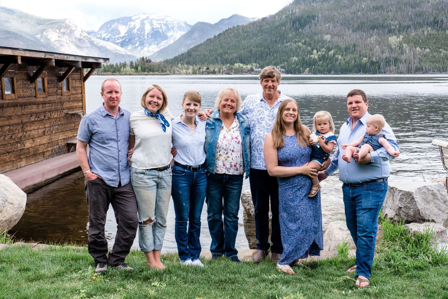 Multi generation family portrait of 7 adults and two children standing on grass off of Shadow Mountain Lake in the mountains of Colorado.