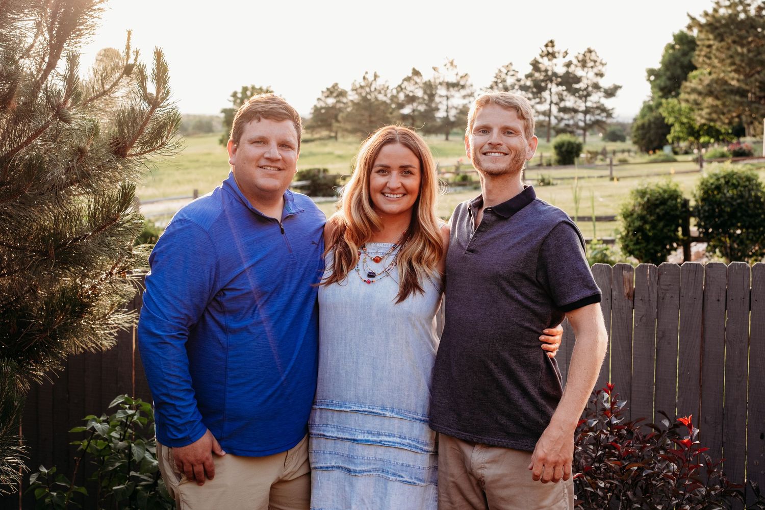 Two adults brothers standing with adult sister in Centennial backyard, all smiling toward camea.