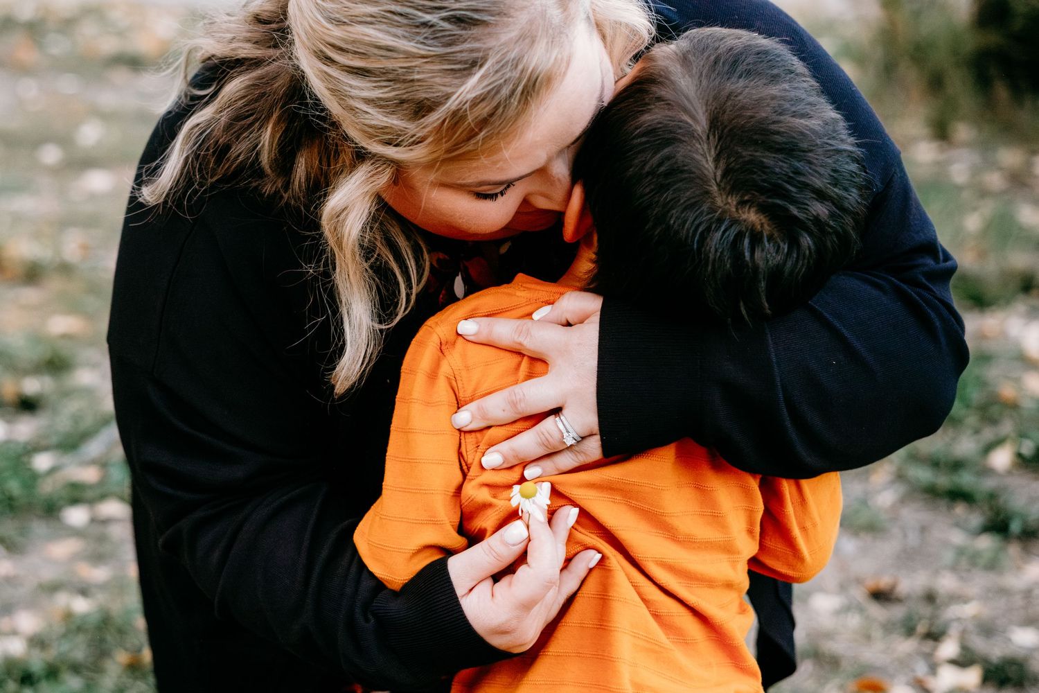 Mother kissing son on the cheek, holding a small flower he had picked for her.