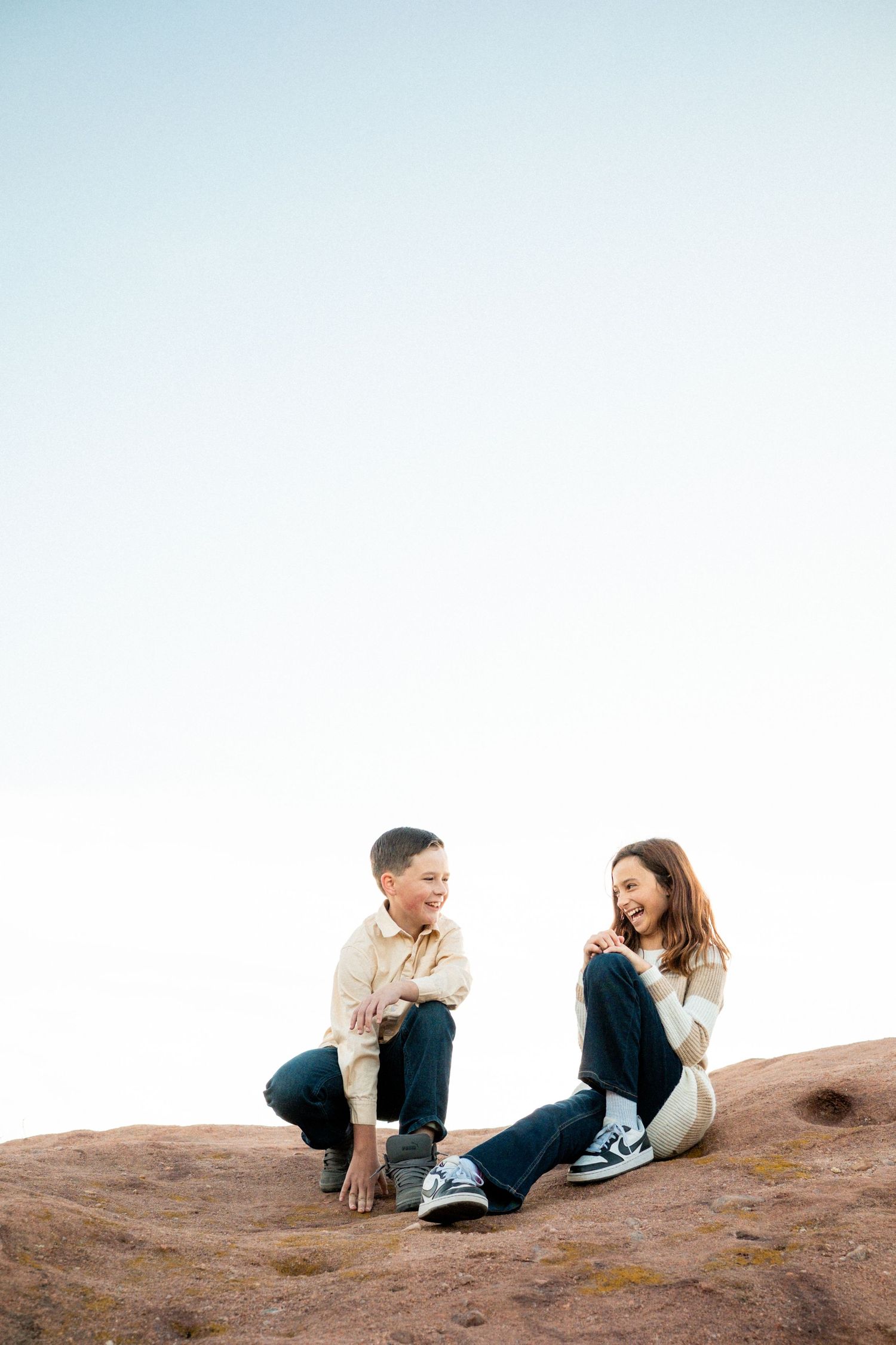 Two tweens sitting on a rock formation, laughing playfully at South Valley Park near Denver.