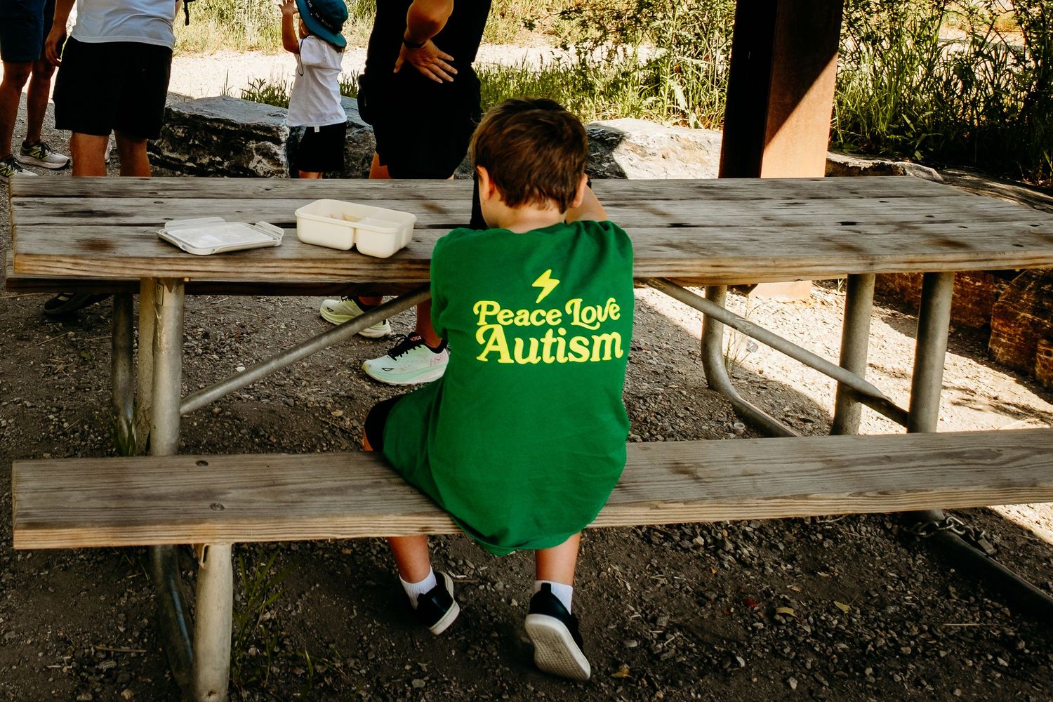 Young boy sitting at a picnic table wearing a shirt that reads, 