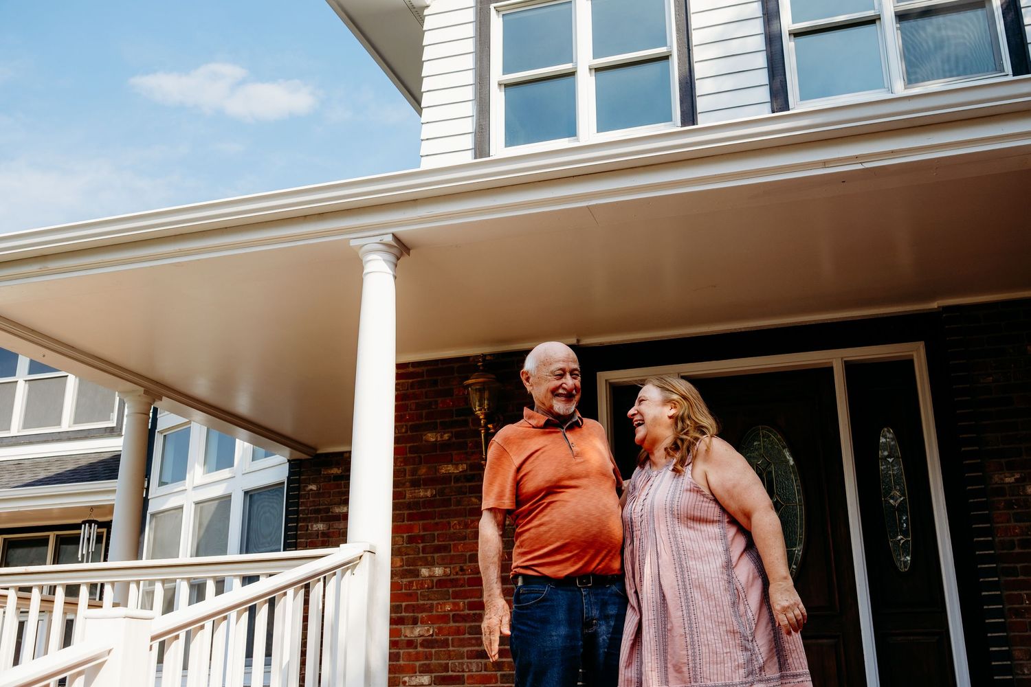 Mother standing with father on family porch, blue sky in background.