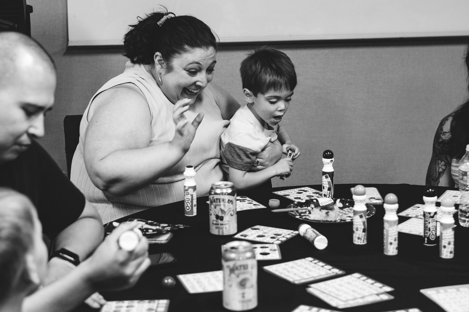 Black and white portrait of family engaging in playfully competitive bingo game in celebration of Grandma's 90th birthday party.