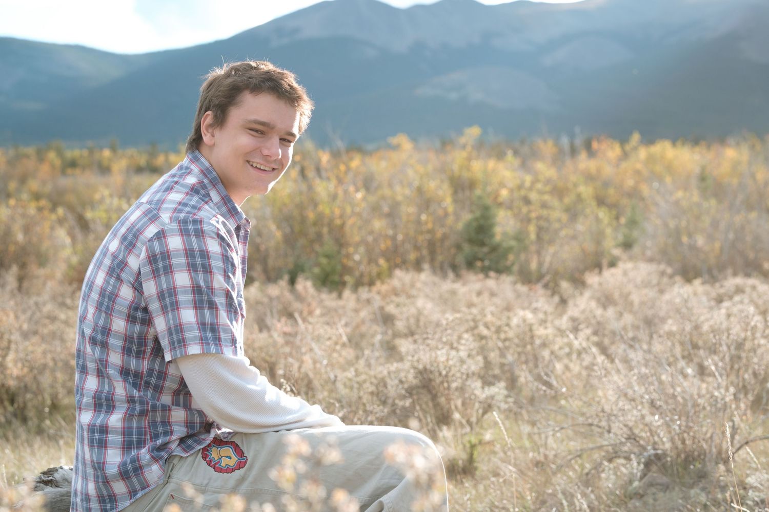 Teen boy sitting in field in Colorado meadow.
