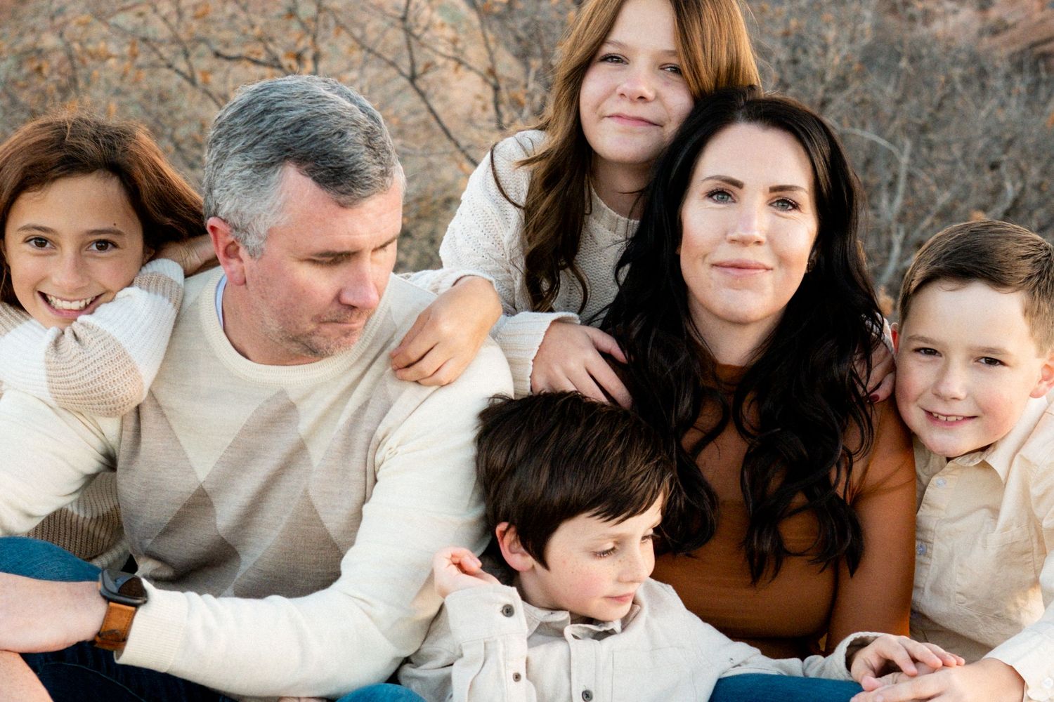Blended family of six all sitting closely together, some smiling at camera, others gazing off into distance.