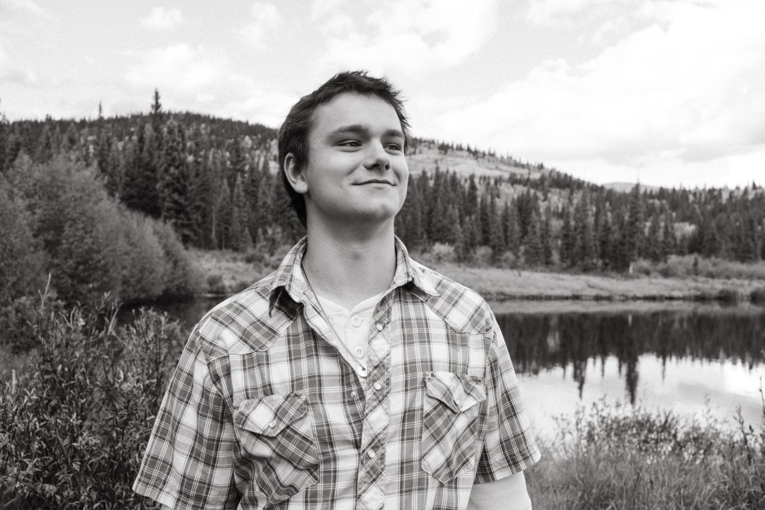 Black and white portrait of teen boy walking in Colorado mountains, smirking.