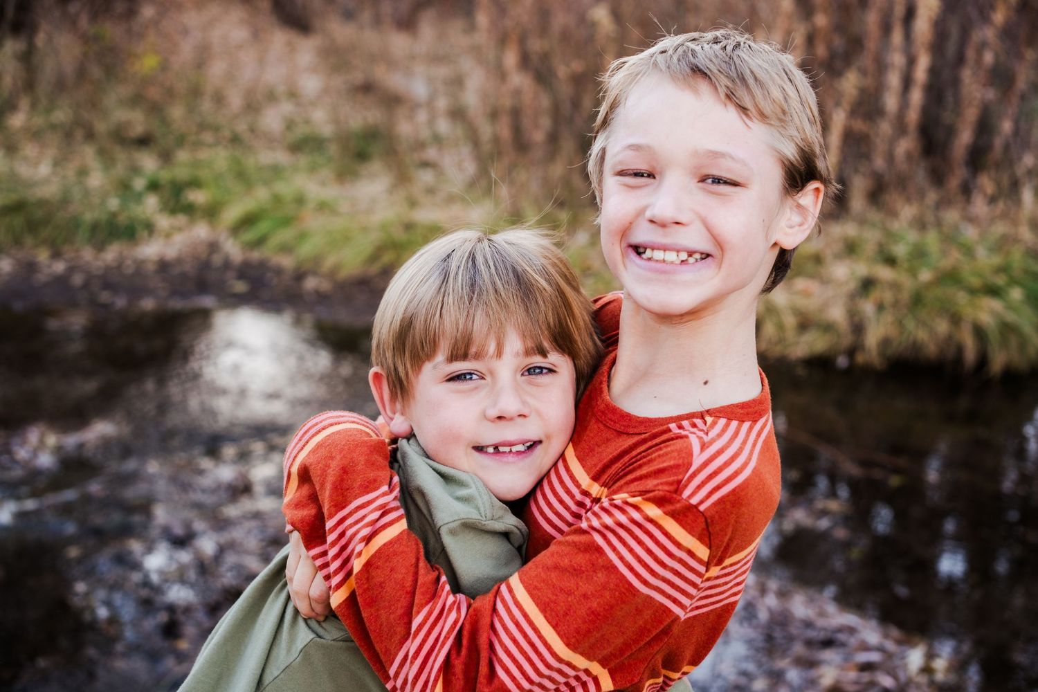 Two brothers smiling beside the creek at Matthews / Winter Park in Golden, Colorado, during a family photo session.