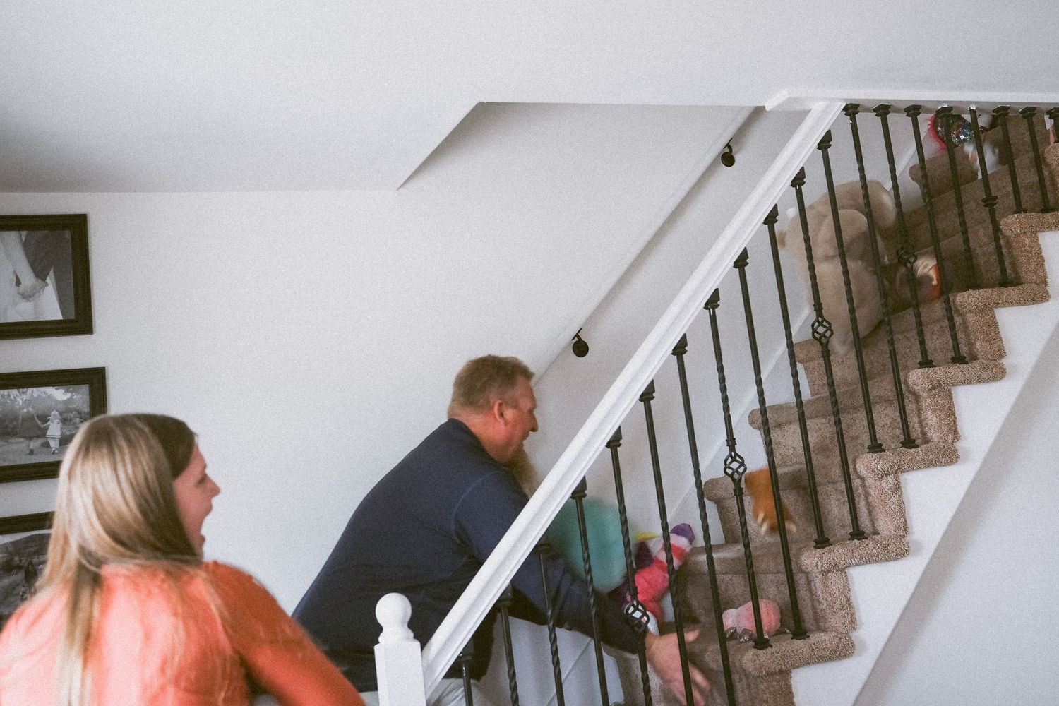 Father and daughter playfully throwing stuffed animals up the stairs.
