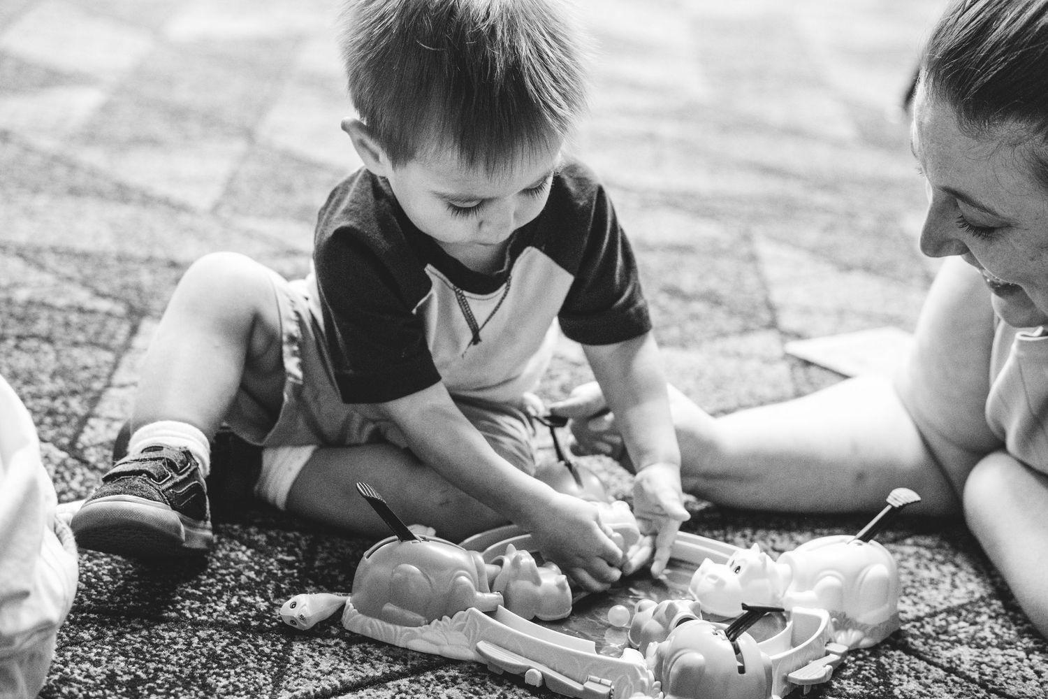 Black and white of young boy playing hungry hungry hippos with aunt.