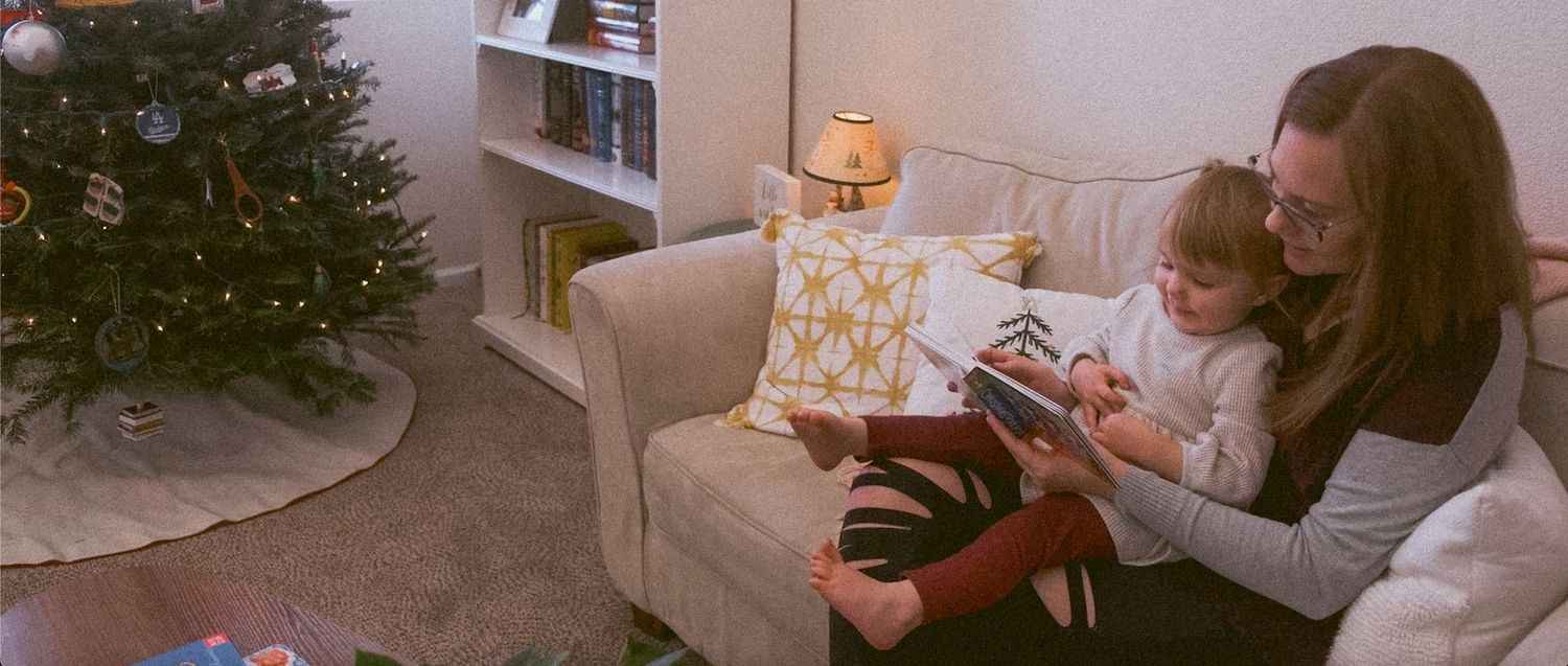 Filmy portrait of mother holding toddler daughter on her lap, reading her a Christmas book.