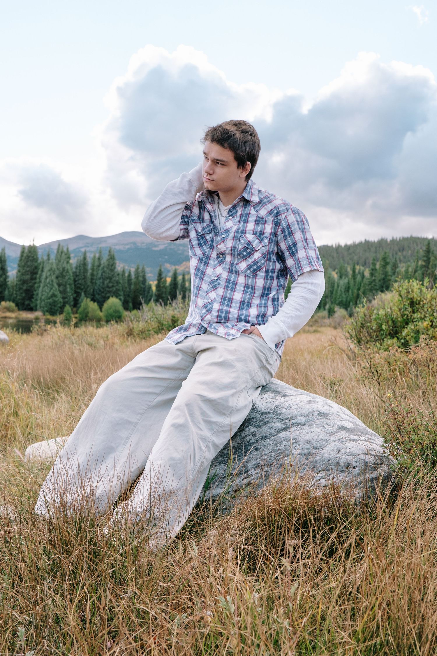 Senior photo of teen boy sitting on boulder in the mountains of Jefferson, Colorado with cloudy skies.