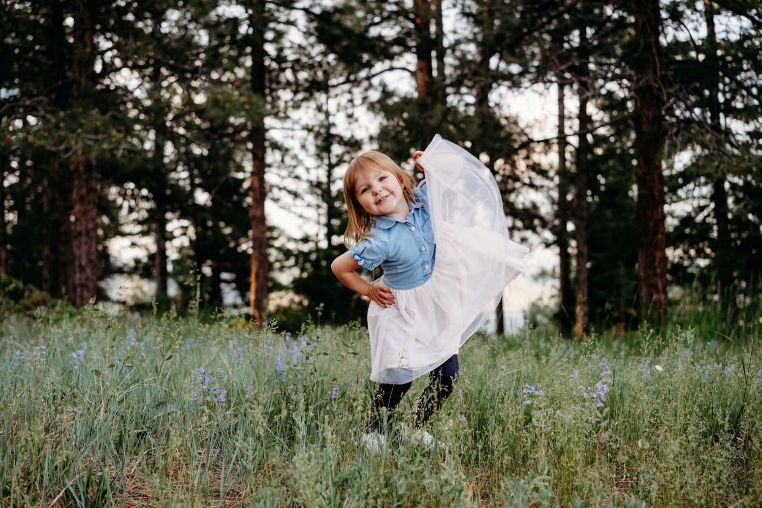 Young girl standing in forest, holding her dress in one hand, other hand on her hip.
