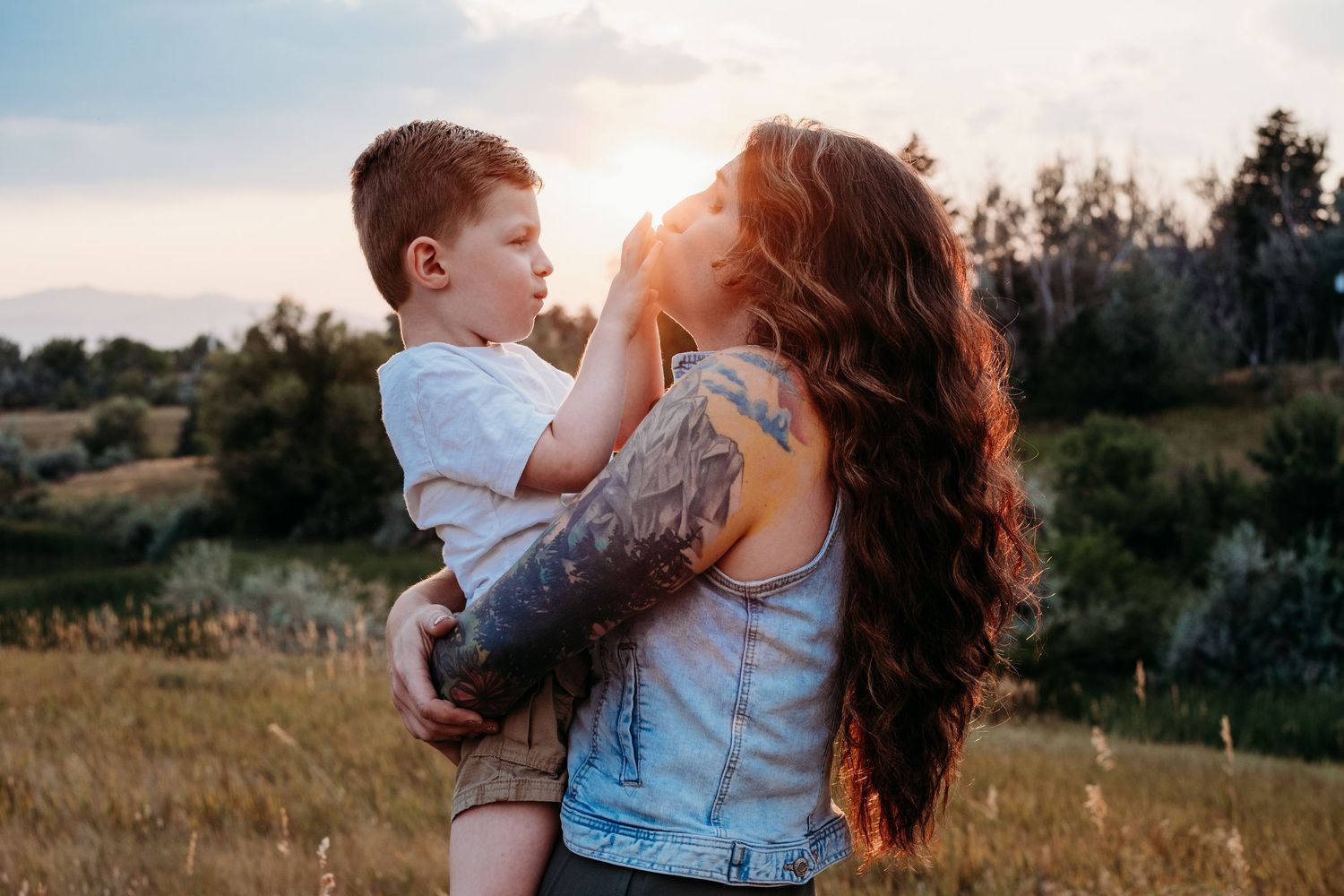Golden hour photography session at Majestic View Park in Arvada, Colorado, mother holding son, kissing his hands, sunshine bursting behind t