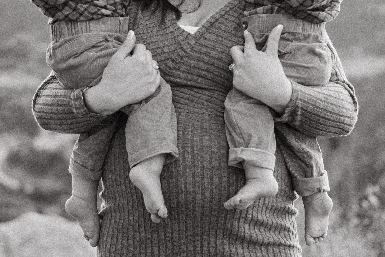 Black and white close up of mother's pregnant belly, holding one twin in each hand.