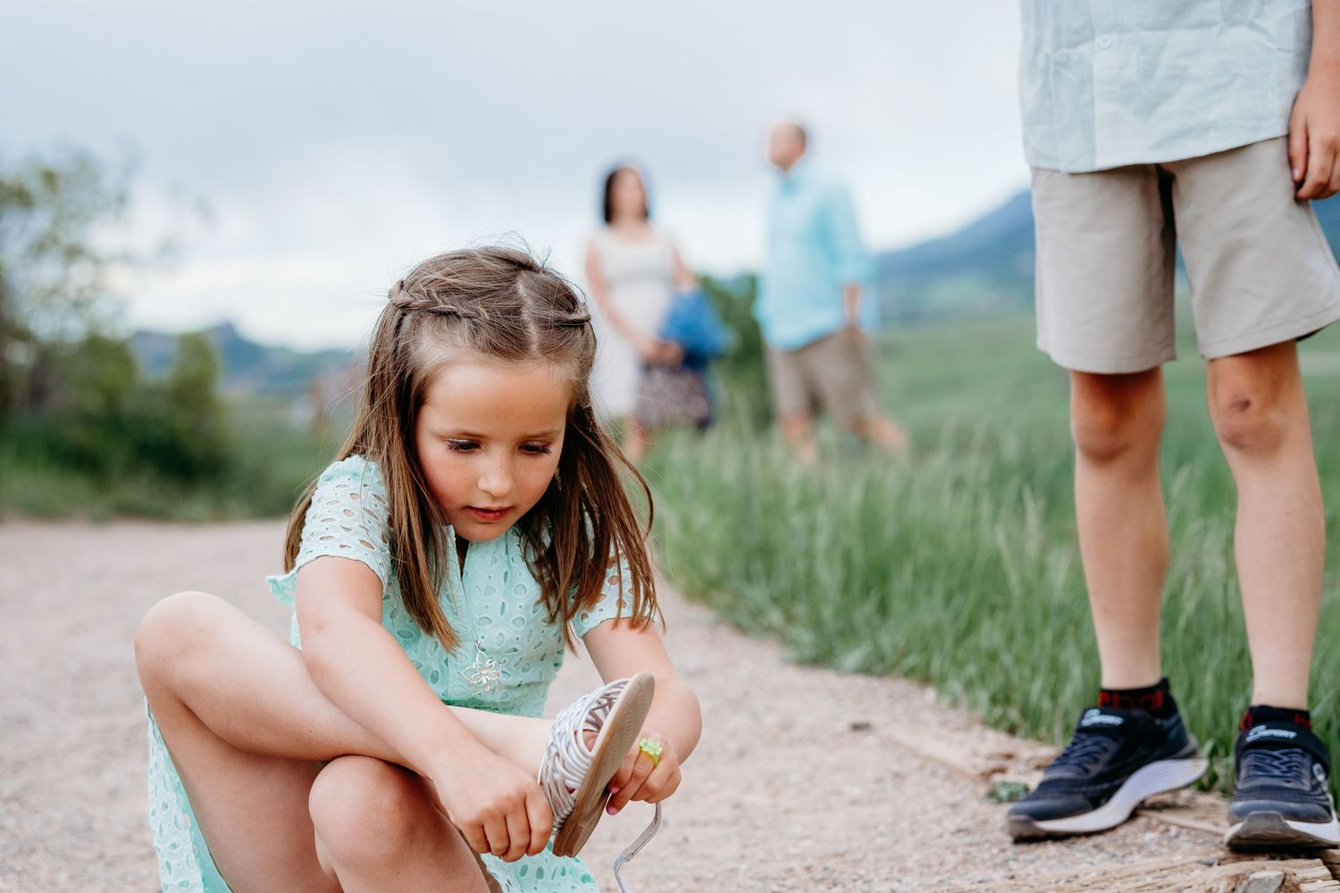 Young girl getting rocks out of her shoe, family standing in background.