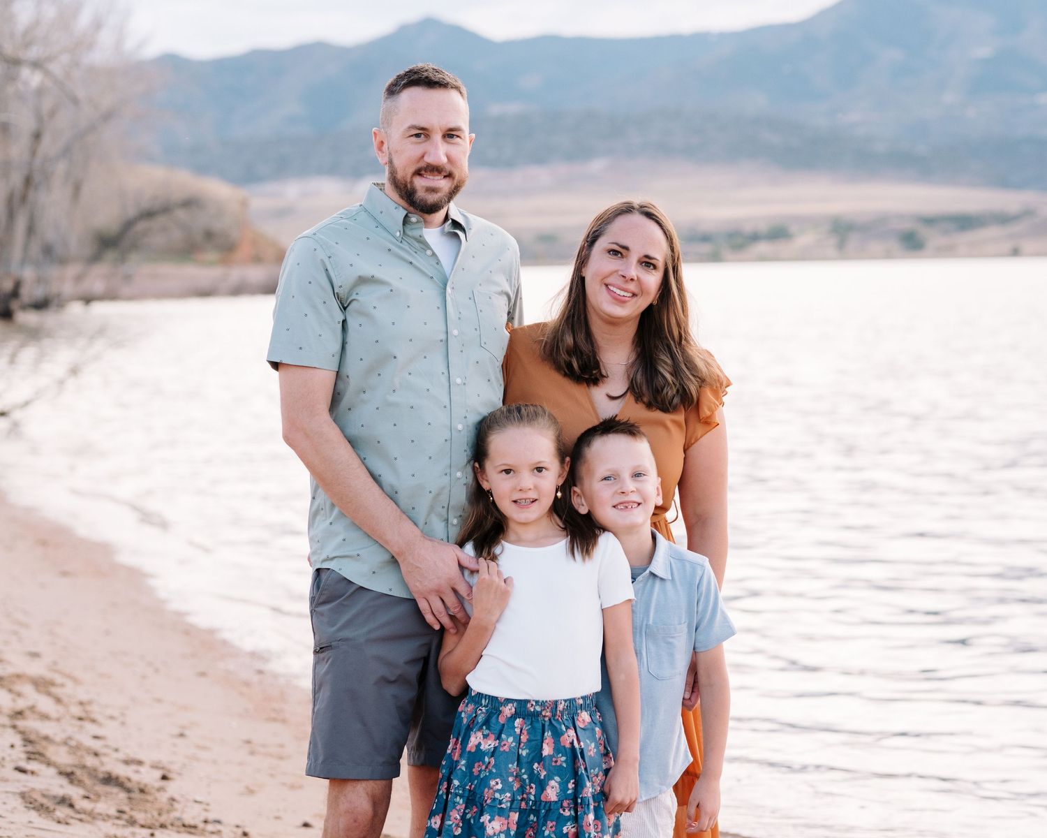 Family of four posing, all smiling, foothills and Chatfield reservoir in background.