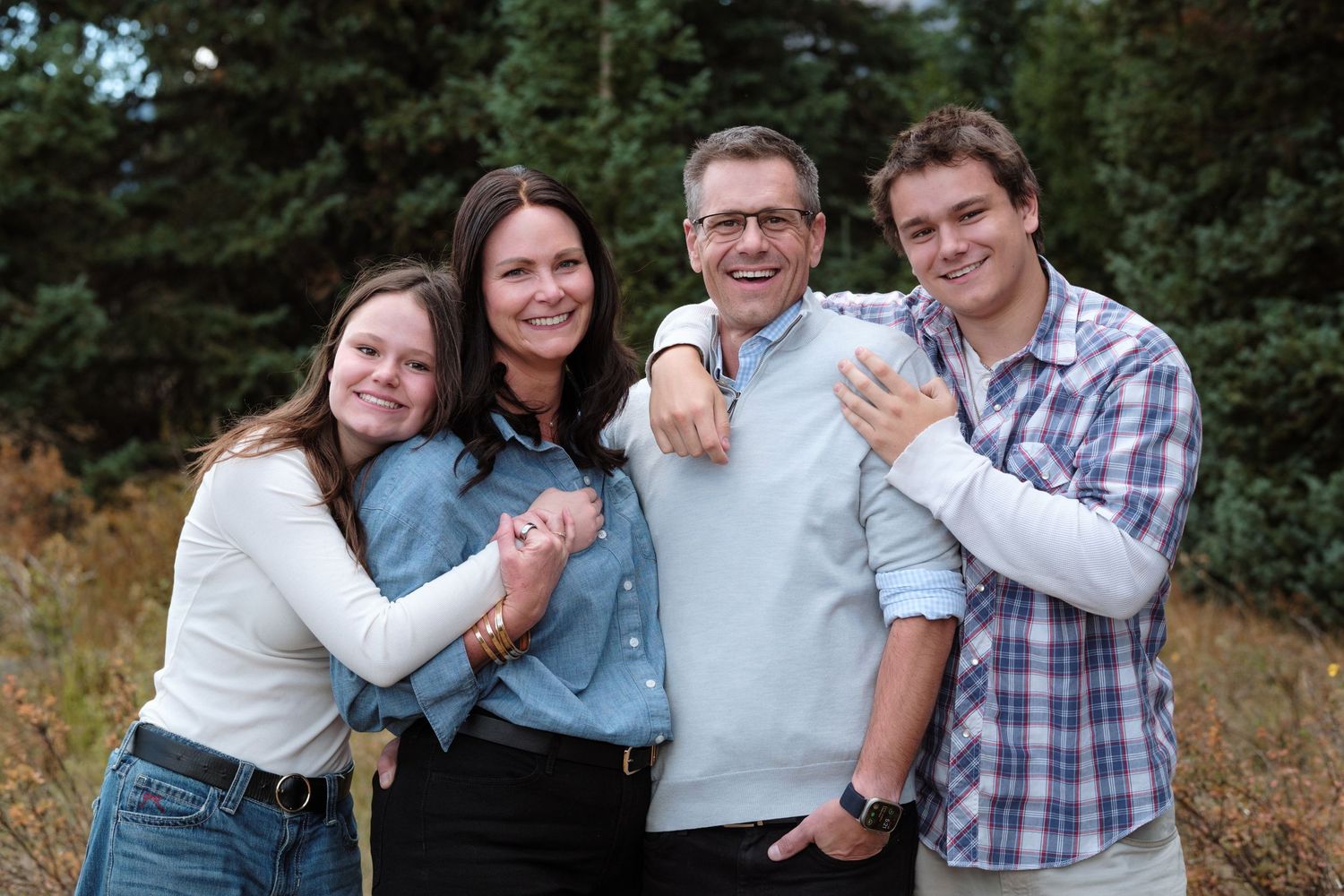 Mother and father standing with teenage children, all wrapping hands around each other.
