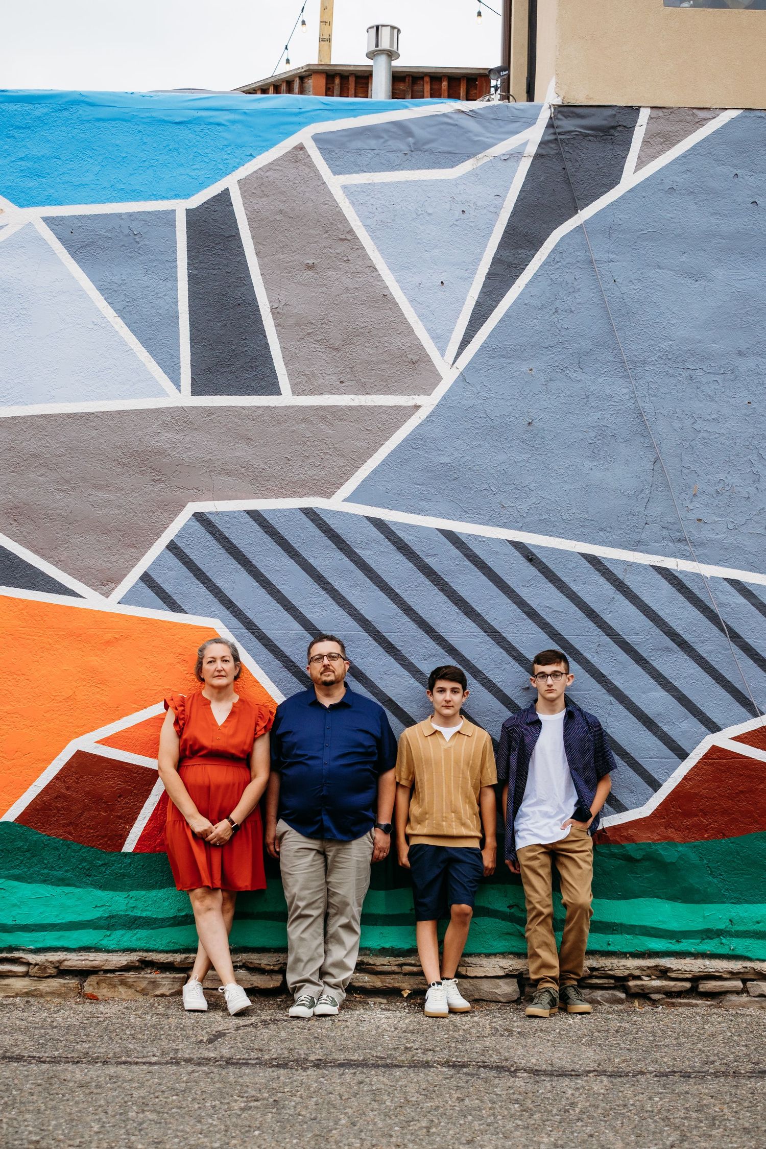 Serious portrait of family of mother, father and two teen sons standing in front of colorful mural in downtown Fort Collins, Colorado.