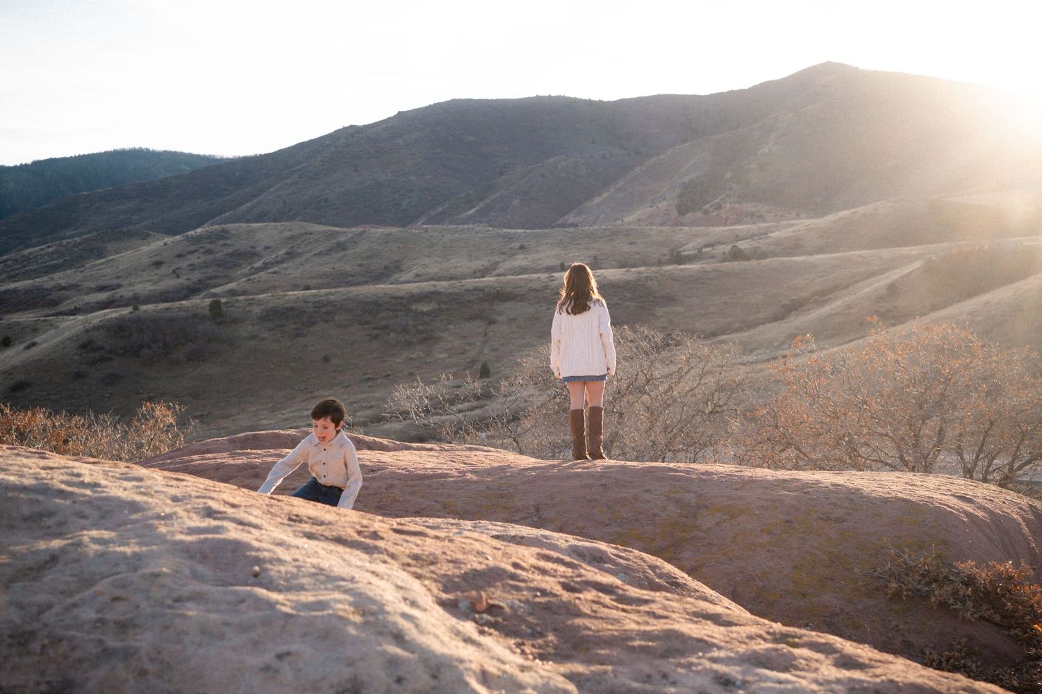 Young boy and tween girl standing in foothills at South Valley Park in Littleton, Colorado.  Sun peaking behind mountain views.