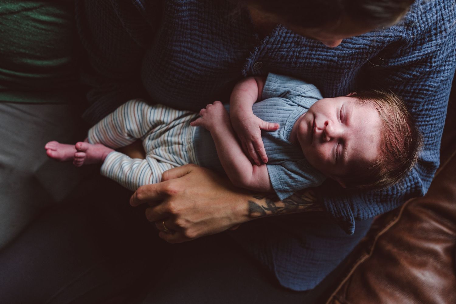 Moody close up of newborn boy behind held in mom's tattooes arms, newborn sleeping.