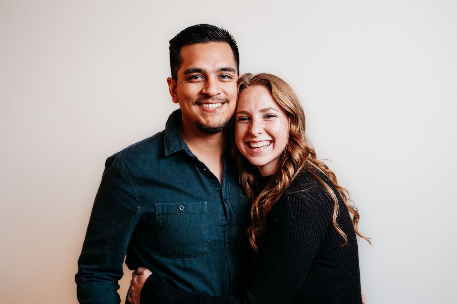 Young couple posed together, both smiling, in studio.
