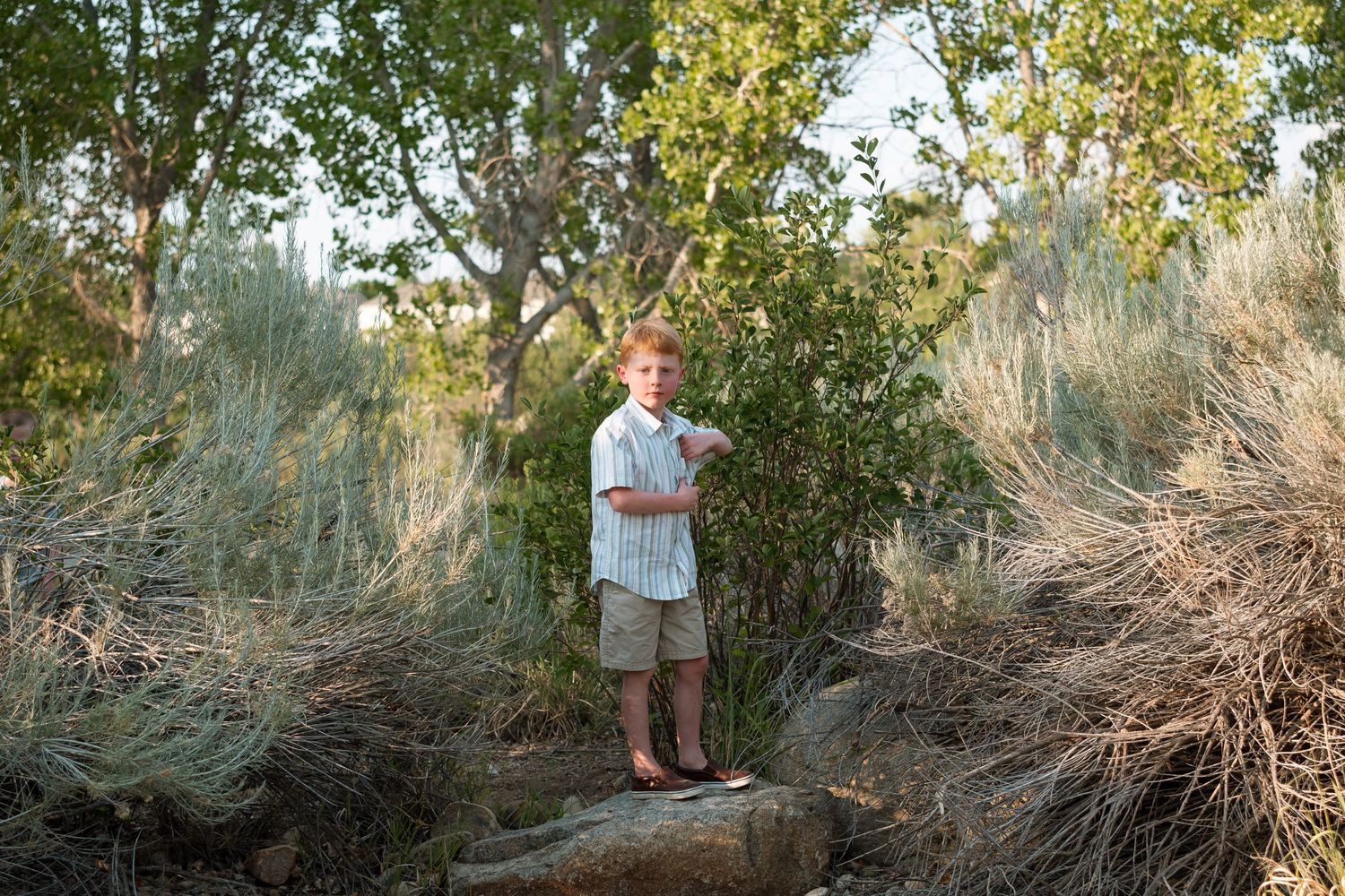 Serious portrait of boy standing on a rock, light illuminating side of his face, staring thoughtfully at camera.