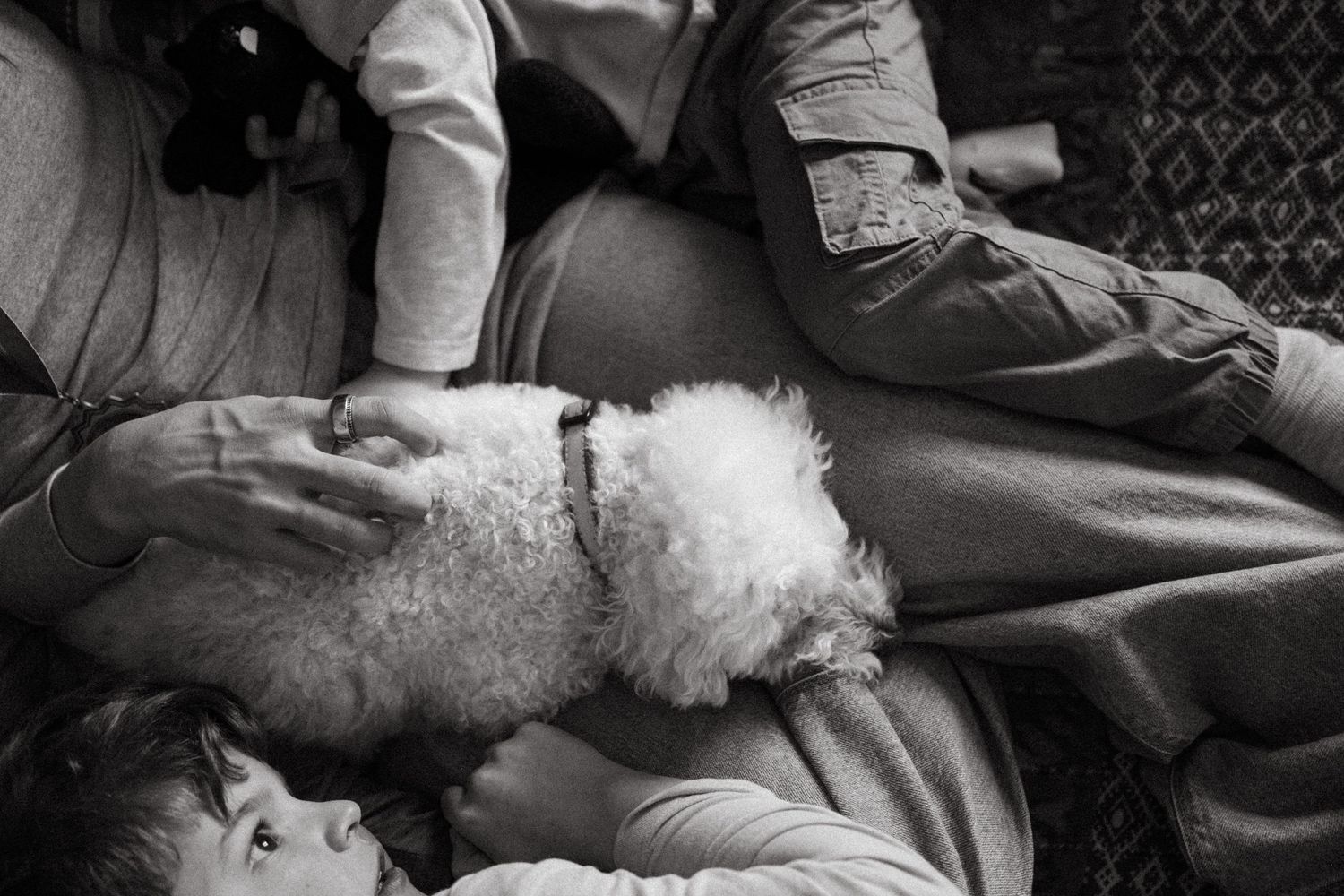 Black and white overhead photo of mother sitting and sons and small, fluffy white dog laying in her lap.