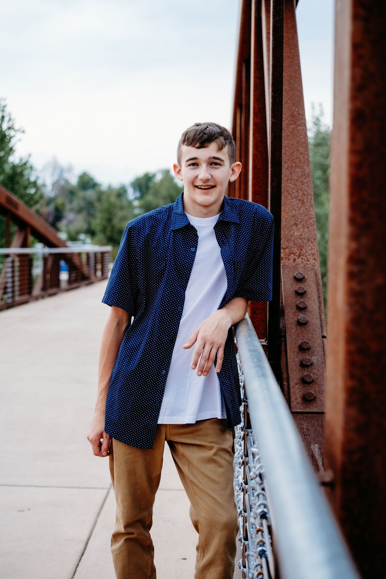 Close up of teen boy near Cache la Poudre river in Fort Collins, leaning against a bridge, smiling.