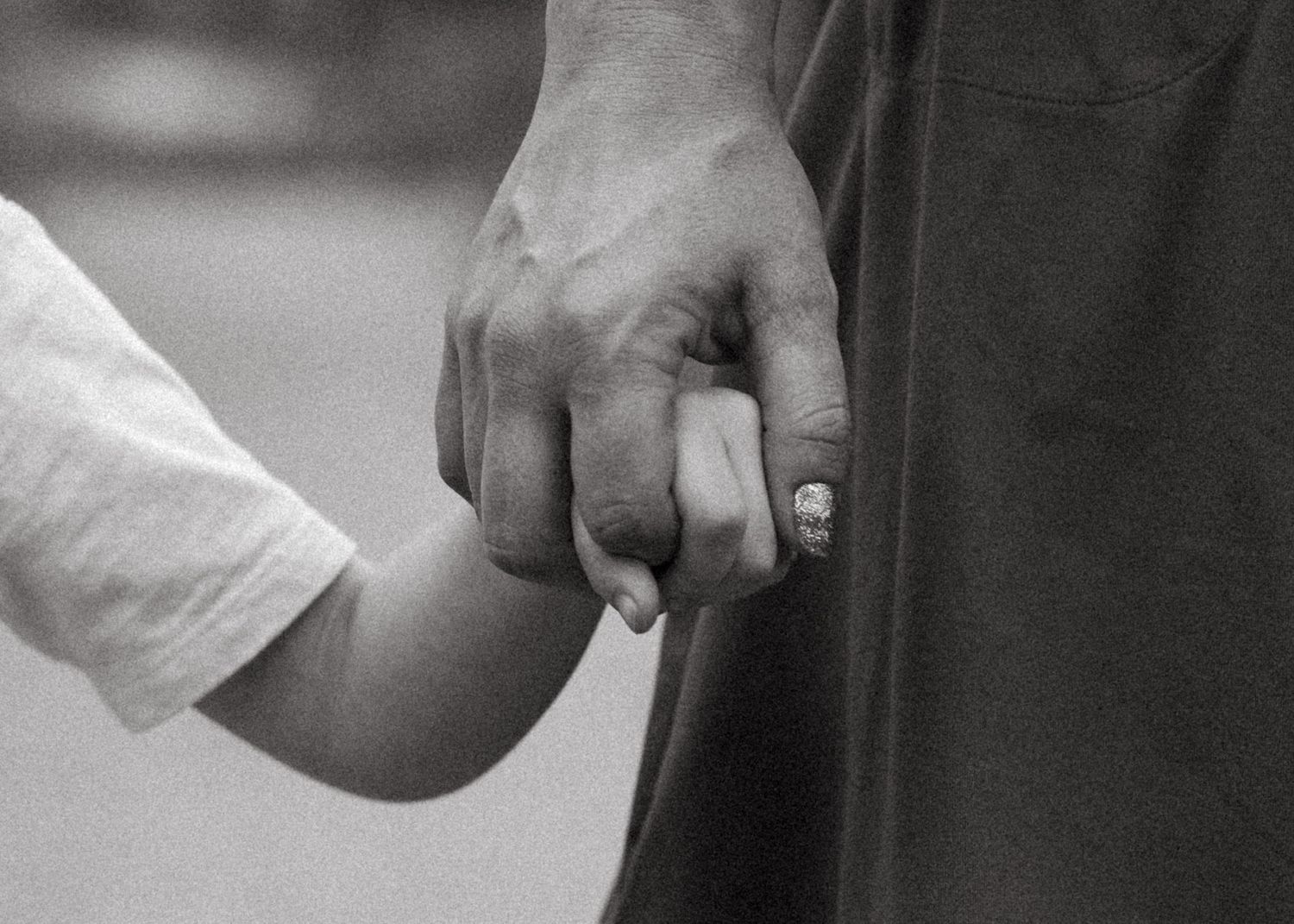 Black and white portrait of son holding mother's index finger in documentary photo session in Arvada, Colorado.